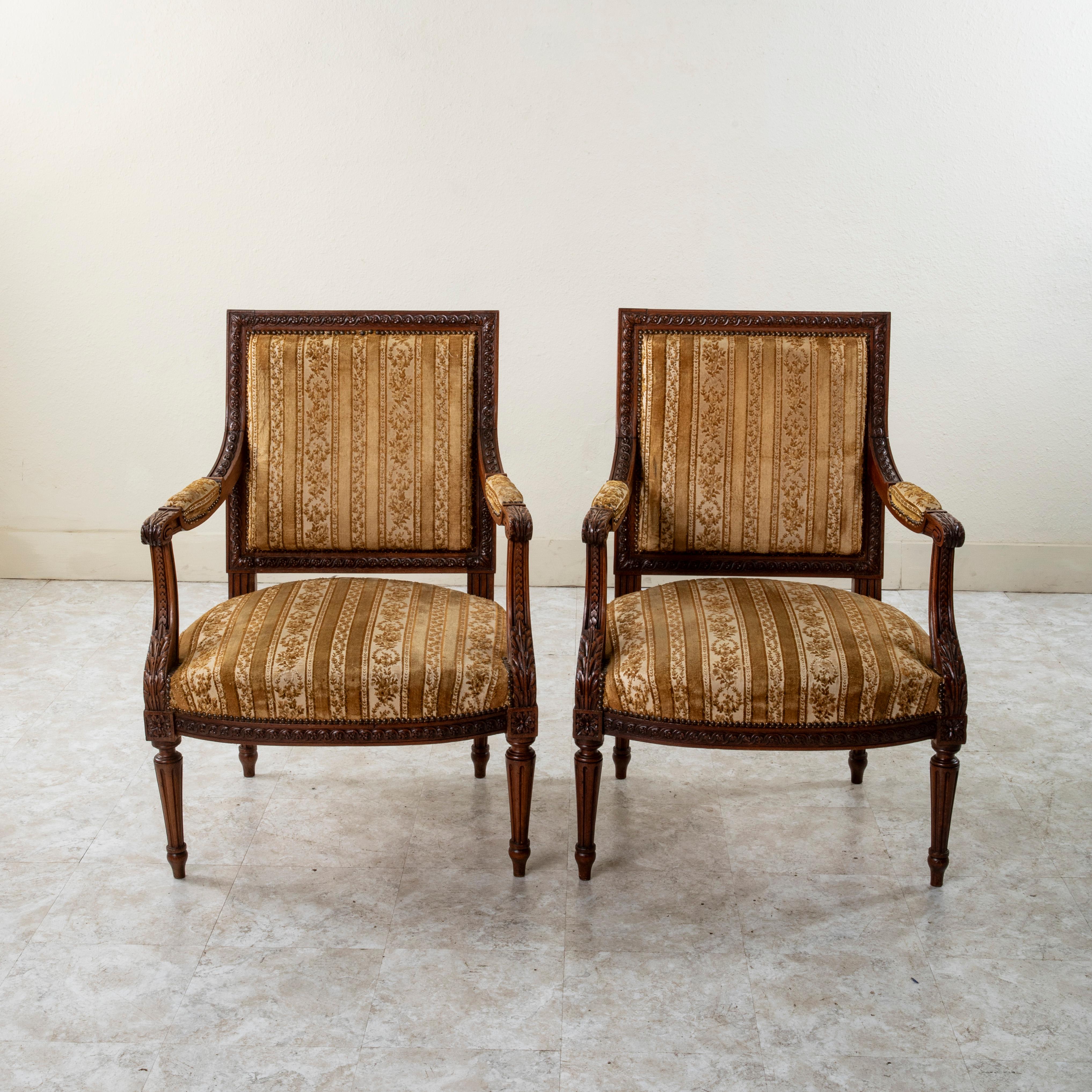 This pair of late nineteenth century French Louis XVI style armchairs is constructed of solid walnut. Their beautifully hand carved details includes classic motifs of an interlaced scrolling and floral pattern, acanthus leaves and overlapping