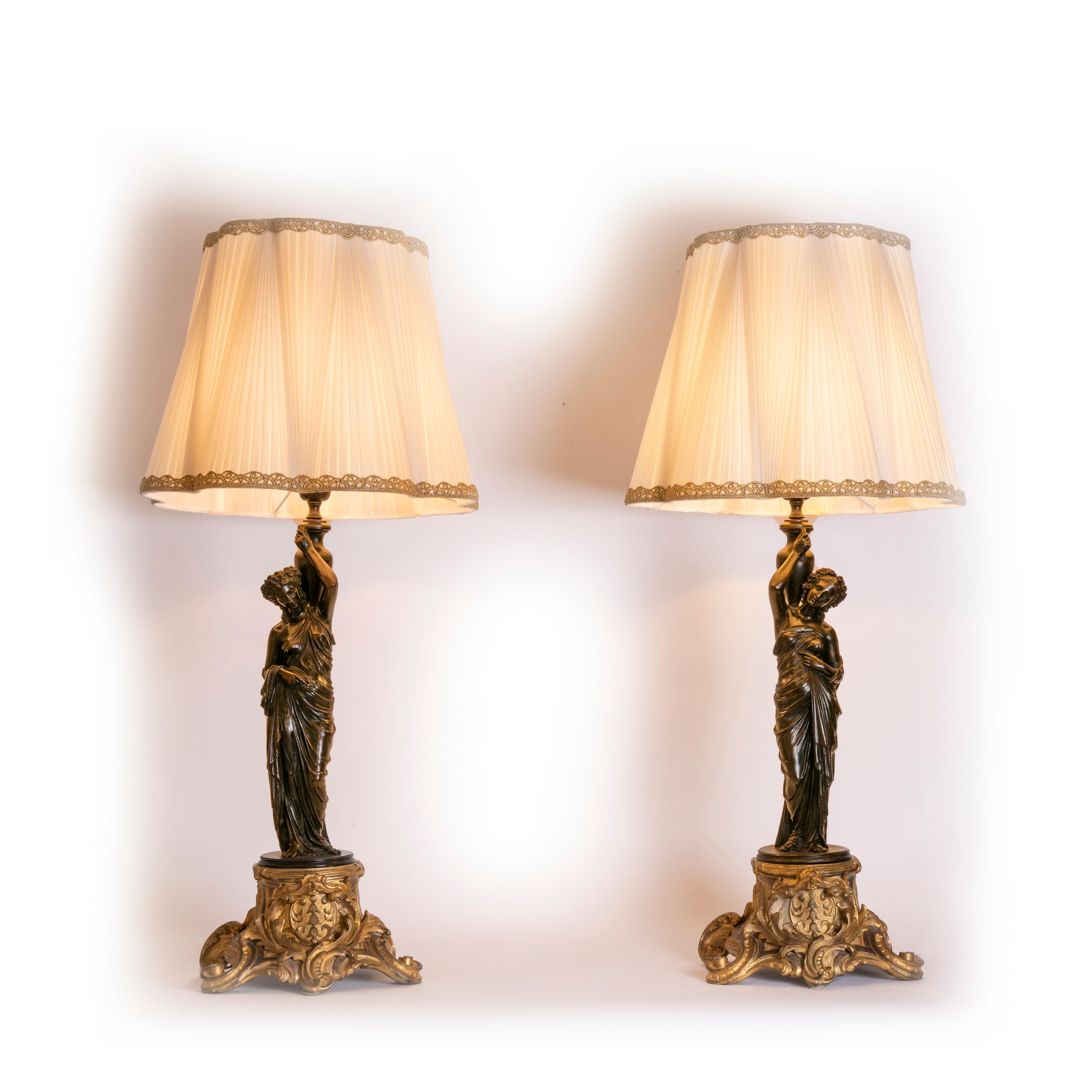 Pair of elegant patinated cast metal female figures of draped classical maidens, figural table lamps modeled as elaborately coiffed and robed neoclassical maidens holding  an amphora on the shoulders and garlands of flowers on the hairstyle.