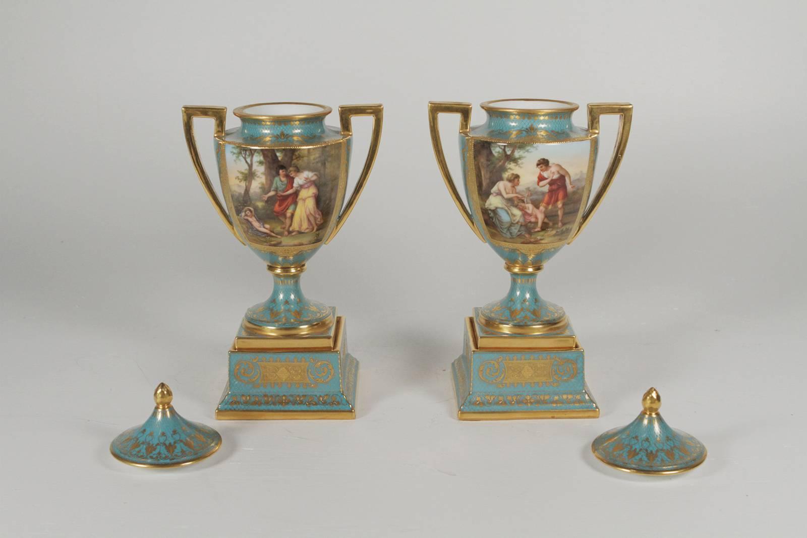 A pair of hand-painted and gilt lidded urns with an Austrian beehive mark on bottom. The unusual robins egg blue background with hand-painted allegorical panels on the fronts. The delicate and elaborate hand gilt details around the panels with