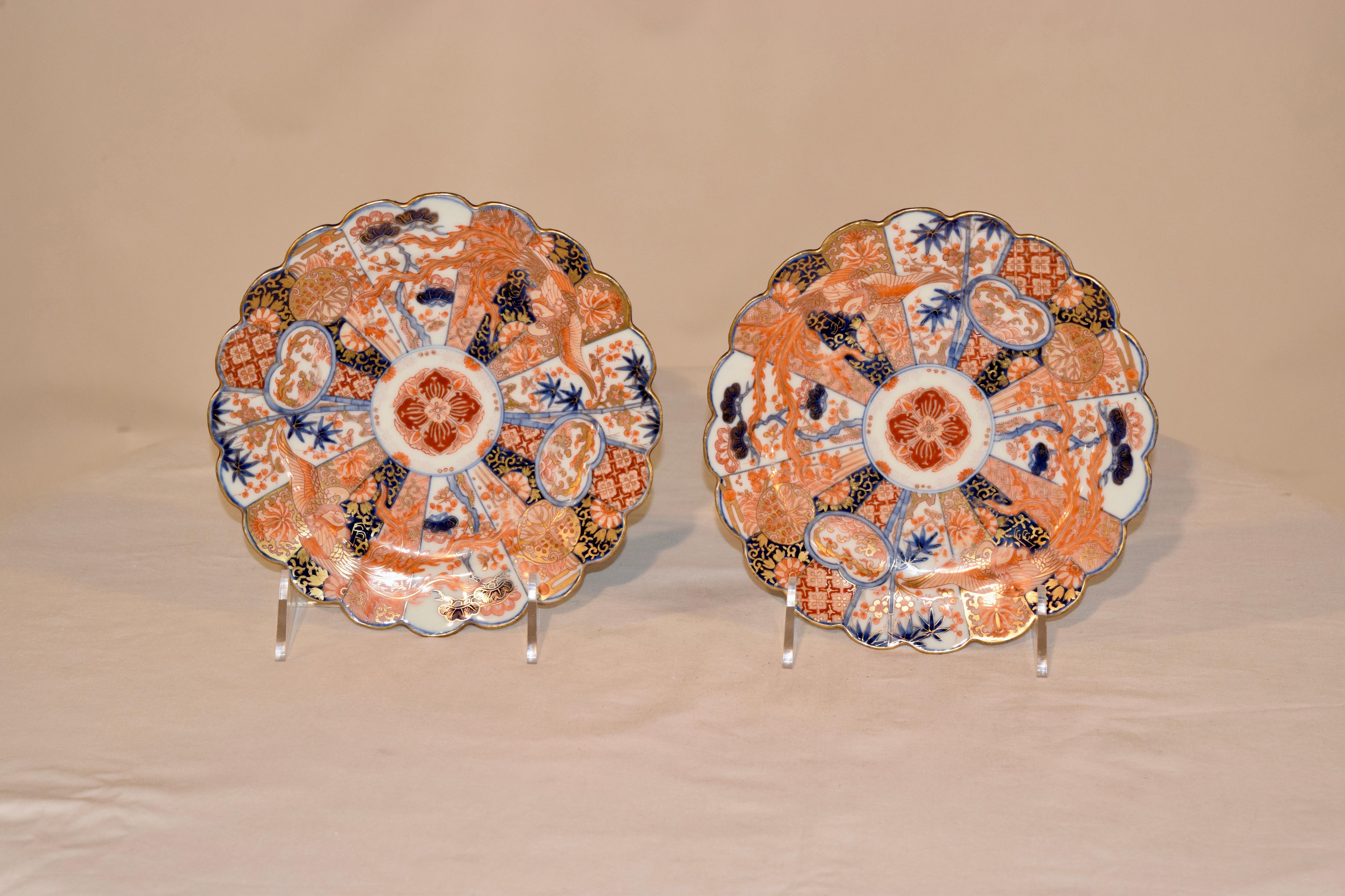 Pair of 19th century Imari plates with scalloped borders that are gilded and have a central medallion with a fan pattern surrounding it, all hand painted with florals and patterns in shades of red, rust, orange and blue. Gorgeous pattern.