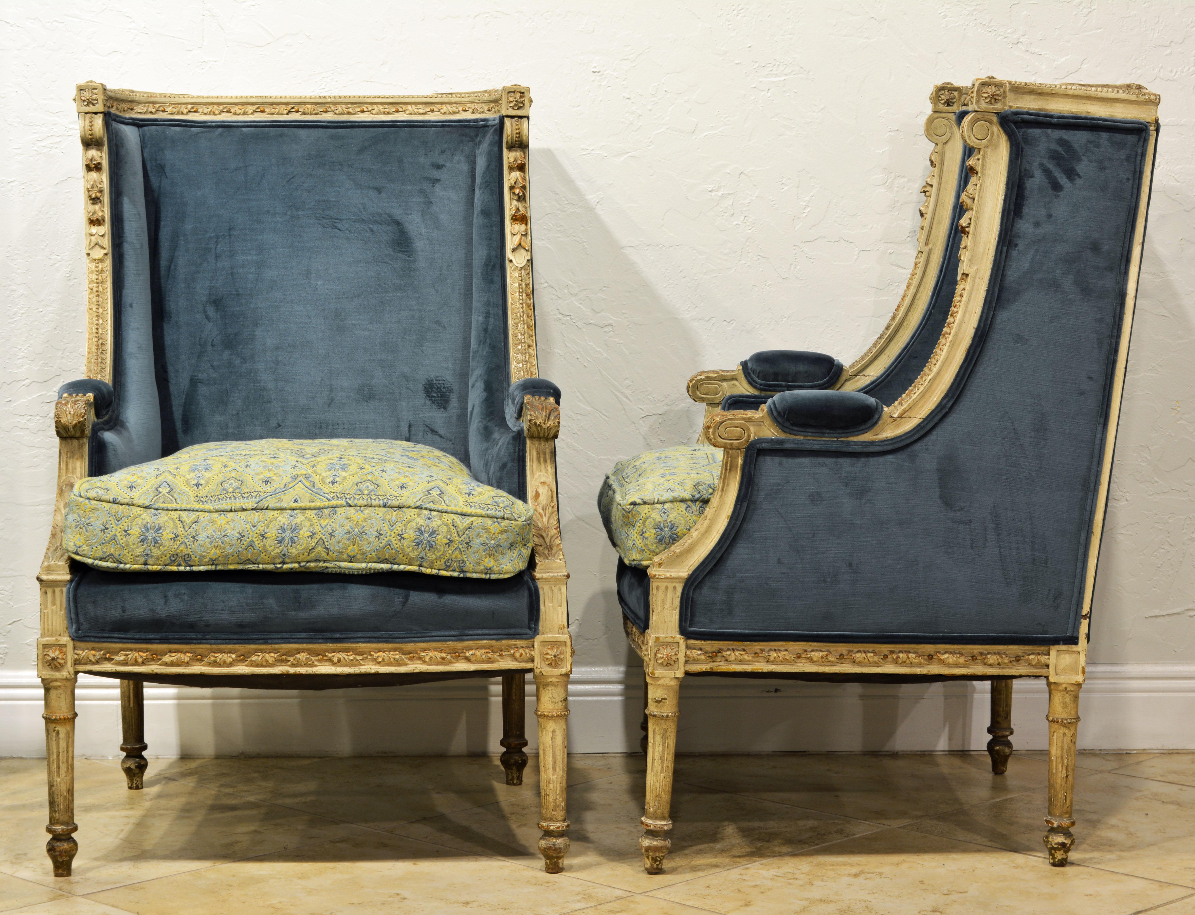 Painted in antique grey/white with small gilt accents and nice wear these well carved bergeres are tastefully complimented by their new cover of blue velvet and matching French pattern cushions.