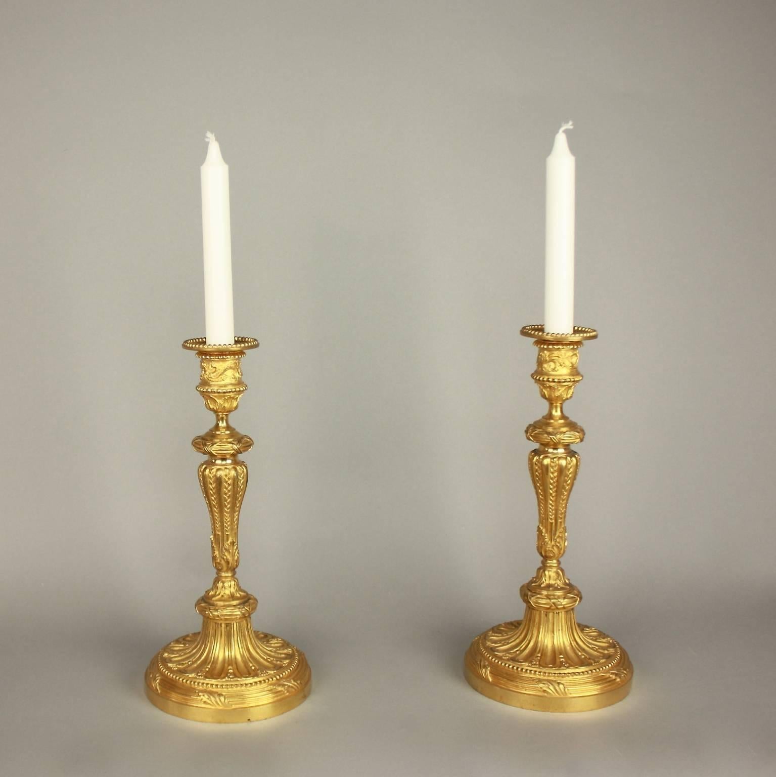 A fine pair of late 19th century Louis XVI style gilt bronze candlesticks, each with a foliate cast nozzle, a fluted tapering stem and an acanthus leaf decorated circular base with ribbon tied garland and gadrooning. Finely cast and chased.