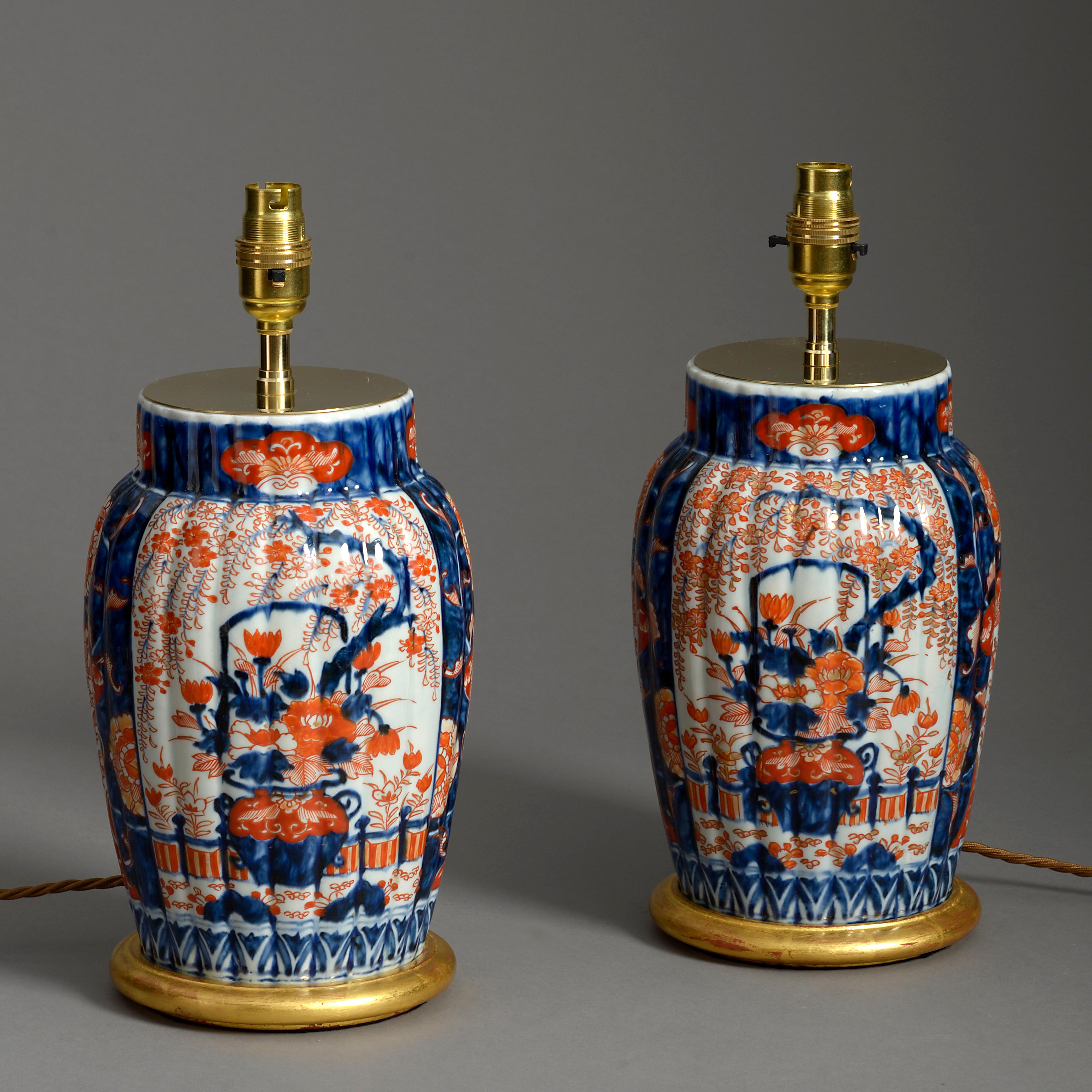 A pair of late nineteenth century Imari porcelain vases, the bodies of ribbed form and decorated with cartouches of flowers and foliage in red, blue and gold glazes upon a white ground. Meiji Period

Now mounted as lamps with hand-turned water