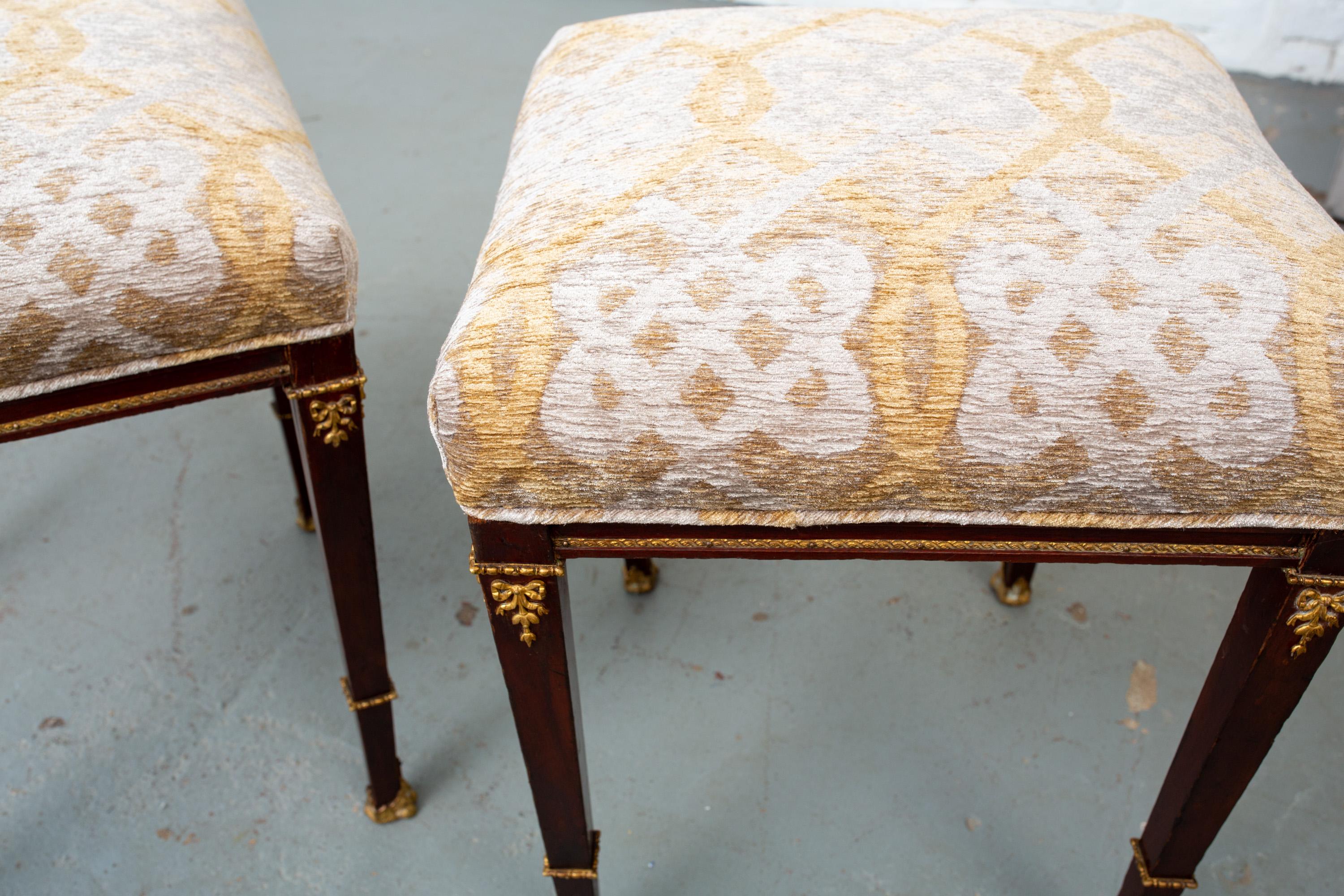 Pair of late 1800s French, neoclassical style foot stools with ormolu mounts and band and bronze claw feet. Newly upholstered. Stools are very structurally sound considering their age.