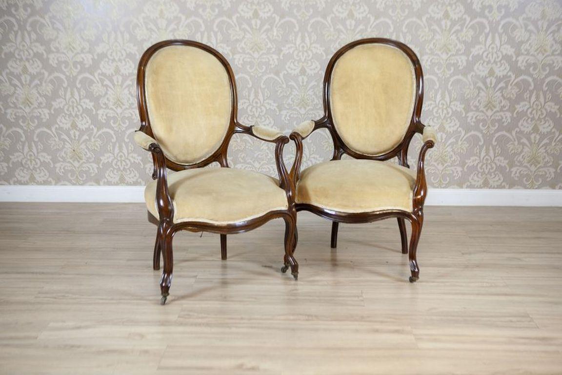 Pair of Late-19th Century Walnut Armchairs in Beige Upholstery

Armchairs with walnut frames upholstered armrests, seat, and medallion-shaped backrest. The chair frames are adorned with fluting. Cabriole front legs culminate in metal wheels.

The