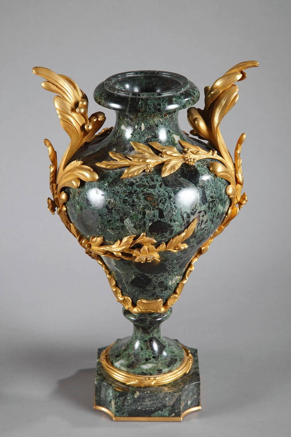 Pair of green marble “vert de mer” baluster-shaped vases. They are richly decorated with gilt bronze Louis XV-style Rocaille, foliage, flowers, and seeds that wind up around the paunch of the marble vases and extend out to form handles. Each vase is