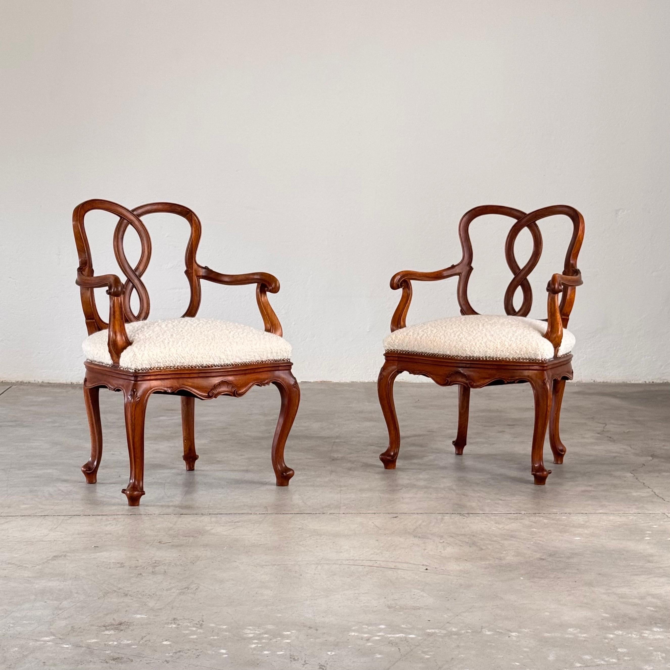 Una refinada pareja de sillones venecianos de finales del siglo XIX, finamente tallados a mano en nogal macizo, totalmente restaurados y reinterpretados con una sensibilidad contemporánea. Los asientos se han retapizado en lujoso bouclé de Dedar