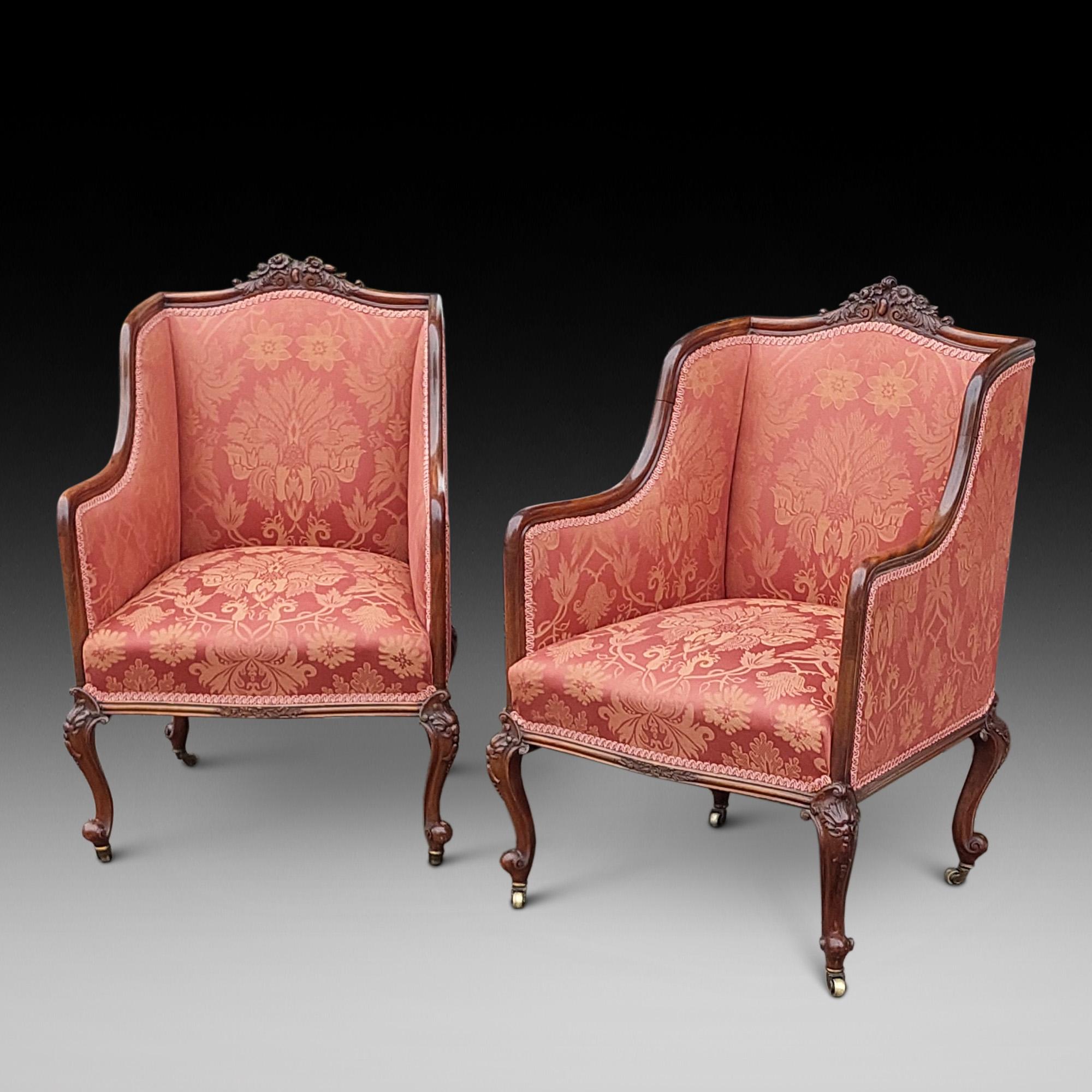 Paire de chaises de salon en acajou sculpté de la fin du XIXe siècle. Chacune avec une traverse supérieure sculptée de feuillages, tapissée d'un tissu à motifs roses, reposant sur des pieds cabriole en forme se terminant par des roulettes en laiton