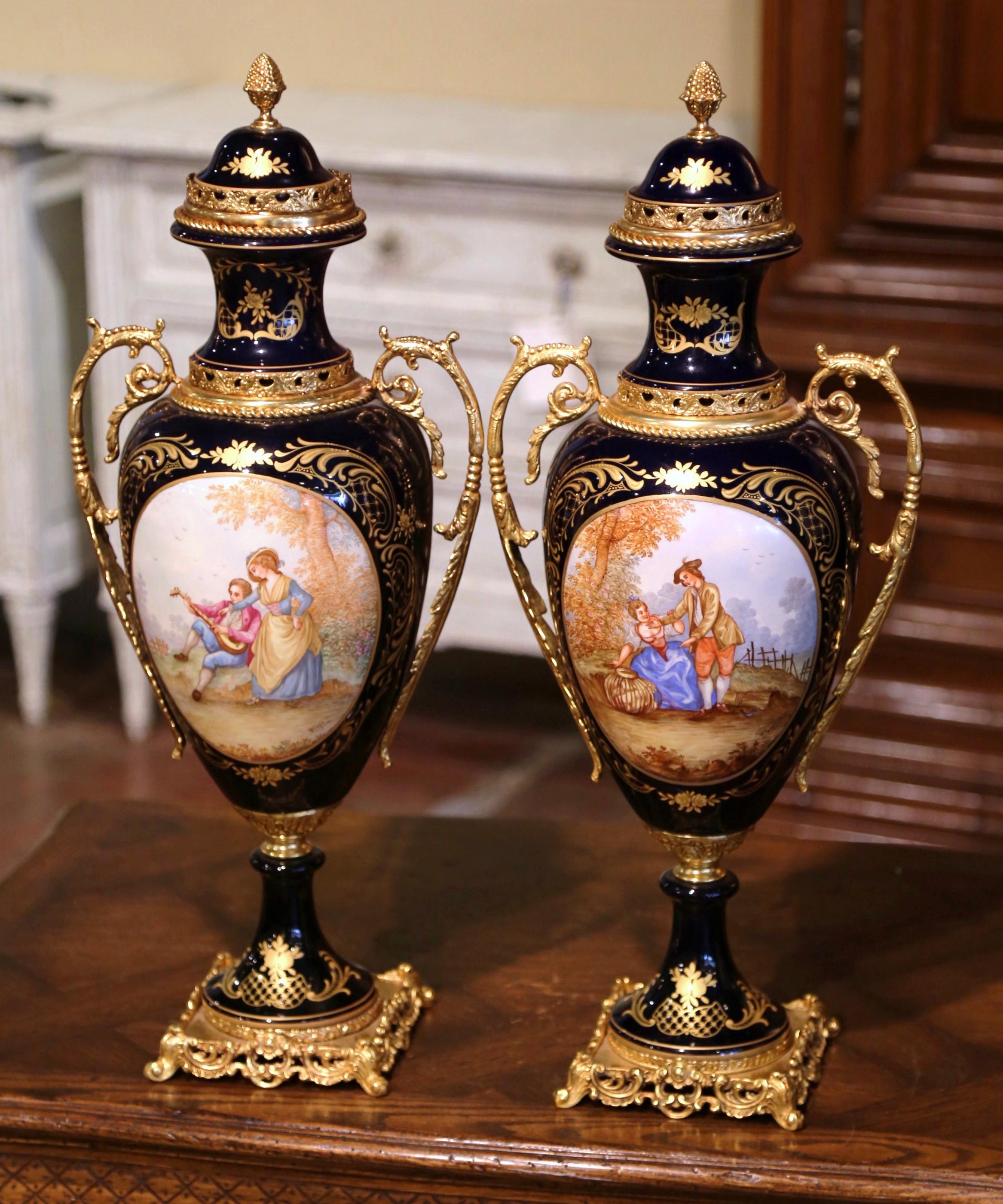 Decorate a mantel or a console with this important pair of porcelain and bronze Sèvres urns. Created near Paris, France, circa 1980, each impressive and elegant vase sits on a square brass base. The vintage urns are decorated with hand painted