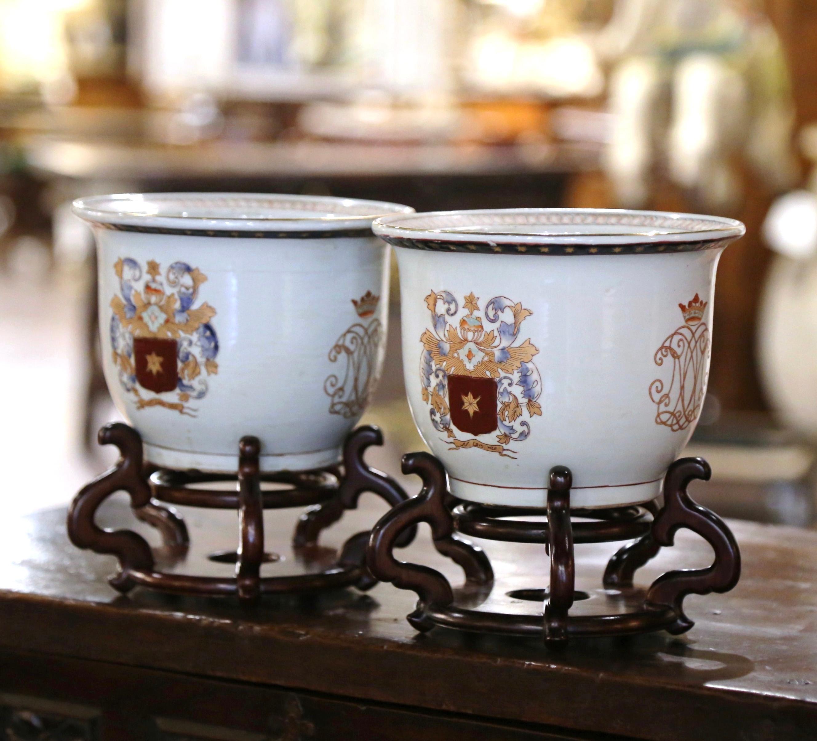 Décorez une cheminée ou une console avec cette élégante paire de vases anciens. Fabriqué en Italie vers 1980, chaque cache pot décoratif en porcelaine est de forme ronde et soutenu par un support en bois. Chaque vase présente deux écussons distincts