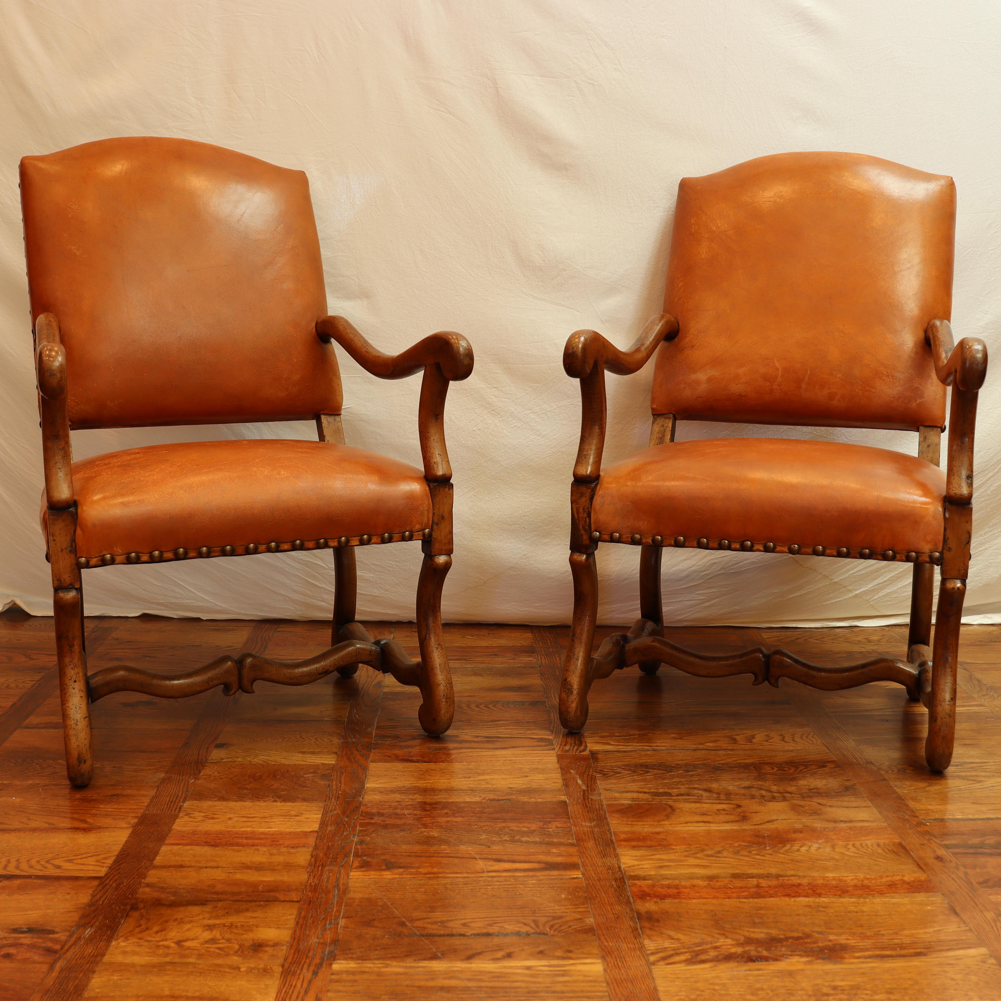 Late 20th Century pair of Louis XIV style style walnut leather upholstered armchairs, each having a shaped back with brass nail head trim, sloped arms, and rising on inswept legs
