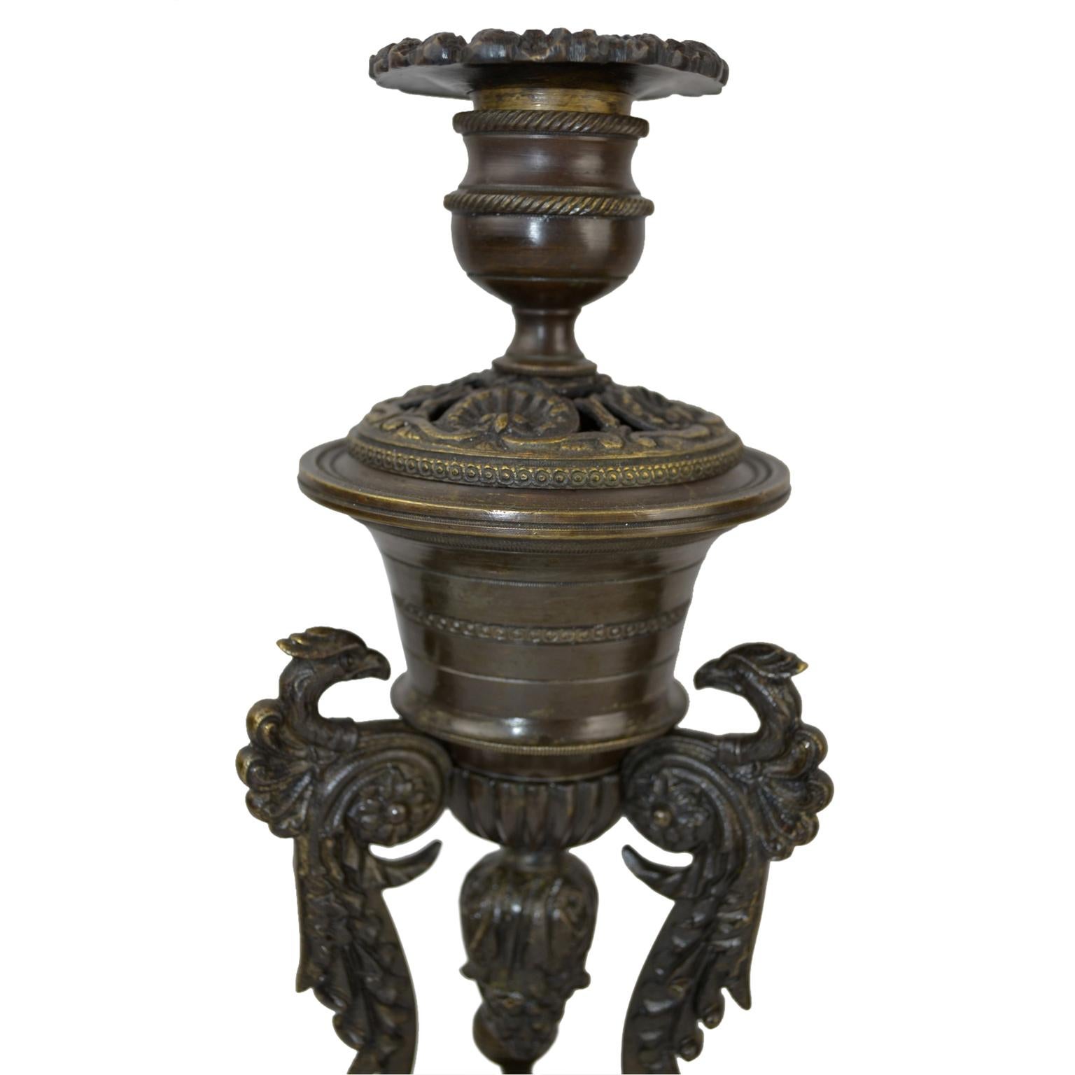 An unusual pair of patinated bronze insence burners and/or candlesticks. The triform base sits on lions paw feet. Each corner of the base supports a stylized winged eagle with one foot on a ball. The eagles in turn support a round tapering 'vase'