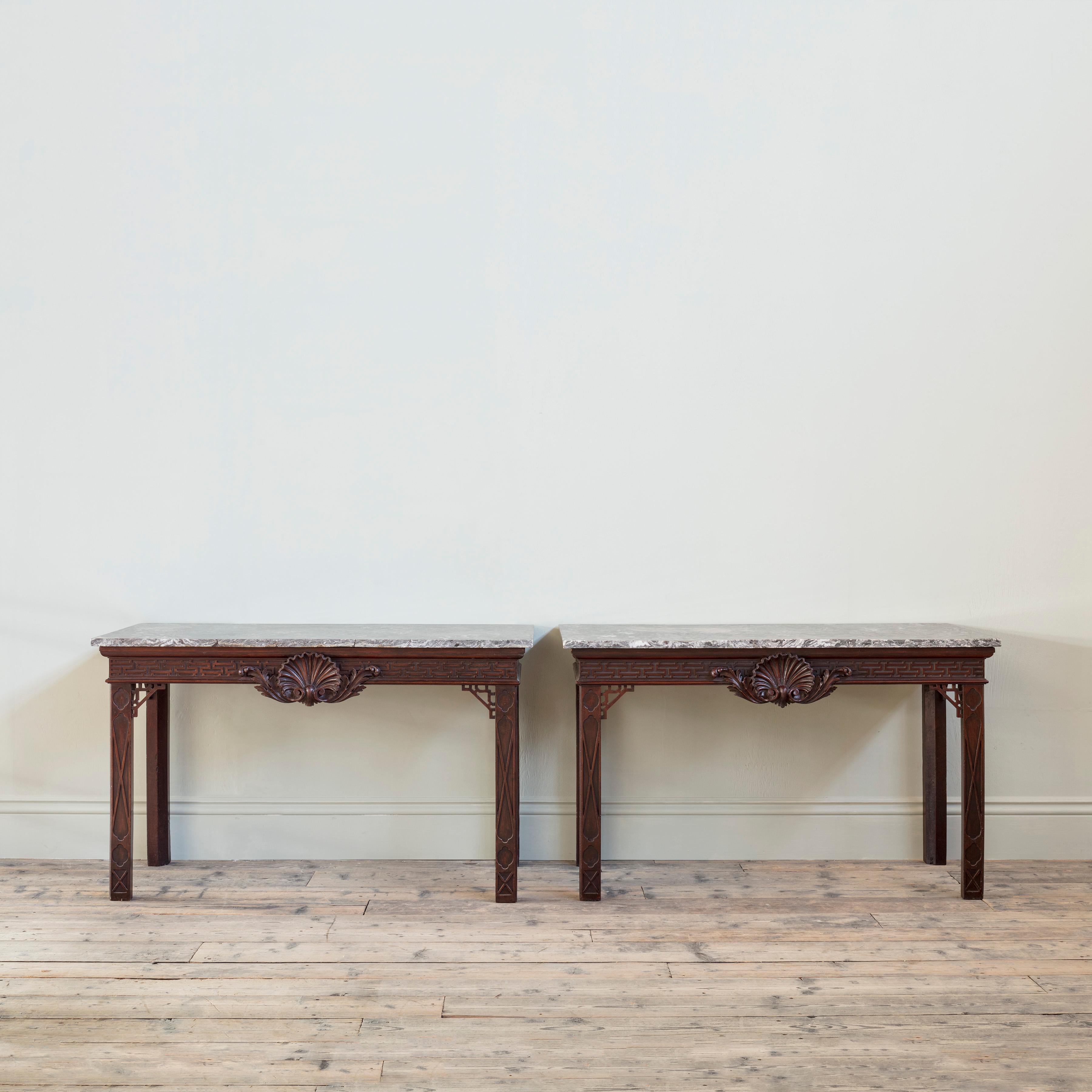 An impressive pair of Late George II mahogany side tables
Possibly by Alexander Peter, circa 1755-1760.

Each with dove grey 18th century marble slab above a geometric key-pattern blind fret-carved frieze, centred by a boldly carved acanthus