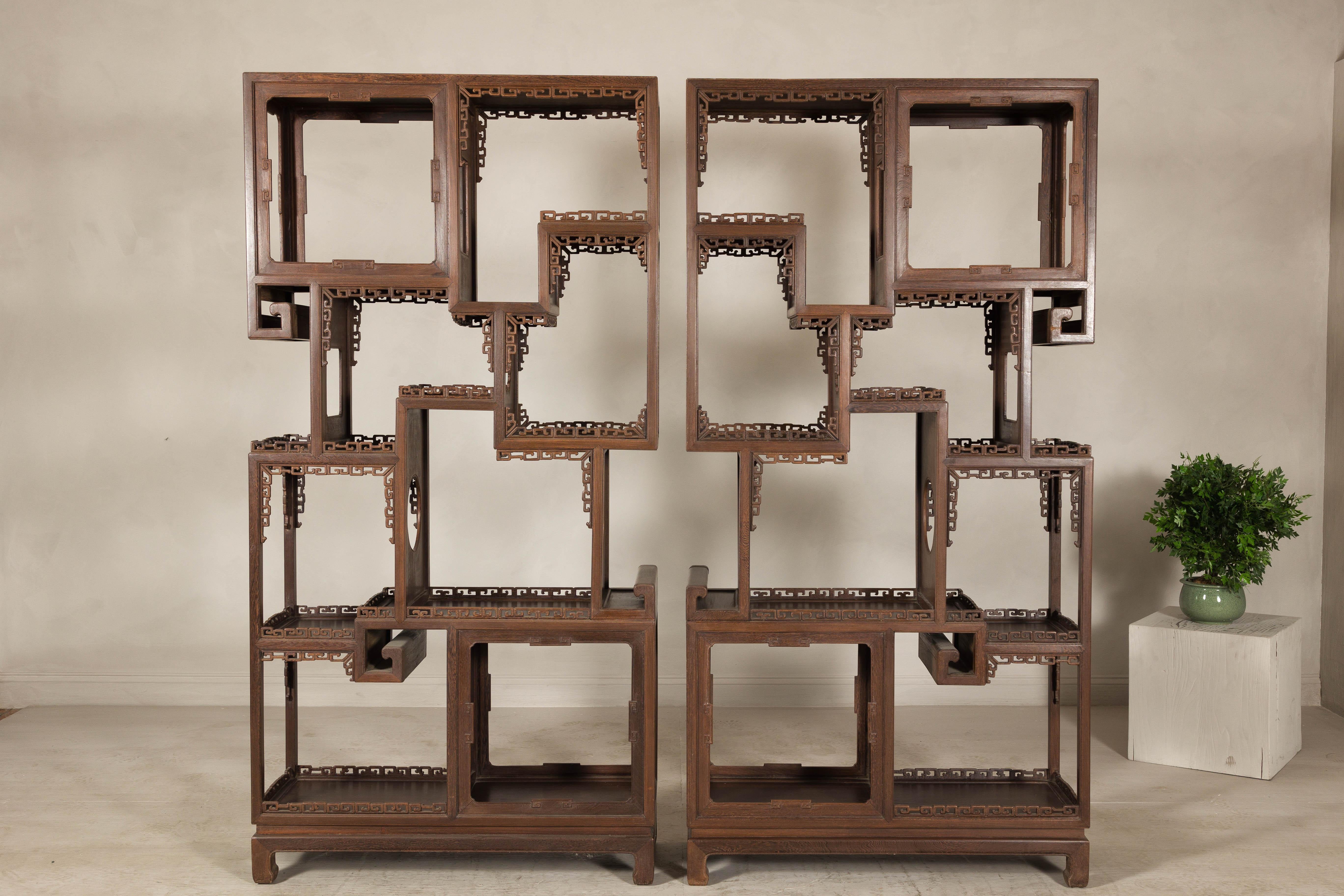 Estas estanterías de finales de la dinastía Qing, un par de estanterías antiguas de madera noble con intrincados motivos calados, realzan cualquier colección con su refinada presencia arquitectónica. El diseño geométrico calado, inspirado en los