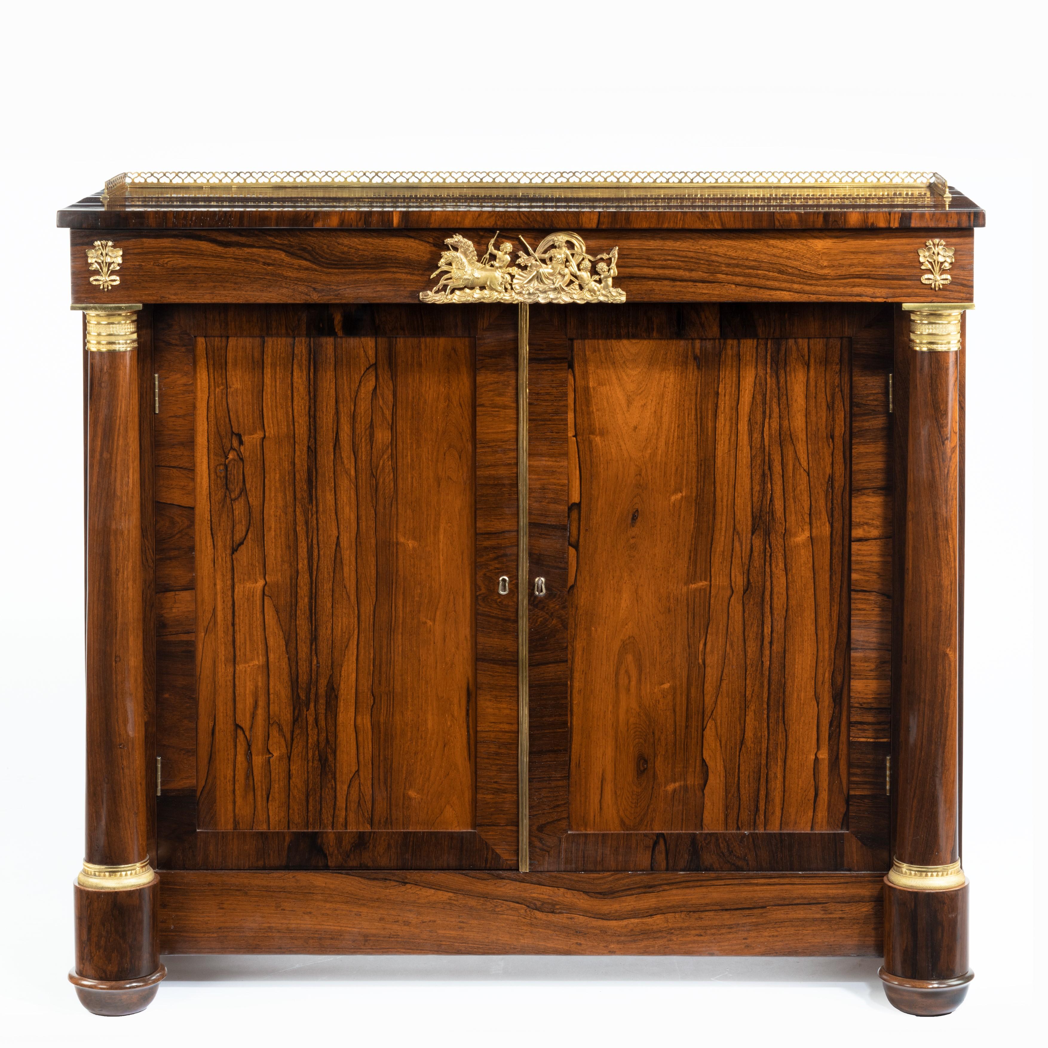 Pair of late Regency rosewood side cabinets, in the French Empire style, each of rectangular form with a disguised frieze drawer and brass gallery above cupboard doors between two tapering pillars, with ormolu mounts depicting the sun-god Apollo in