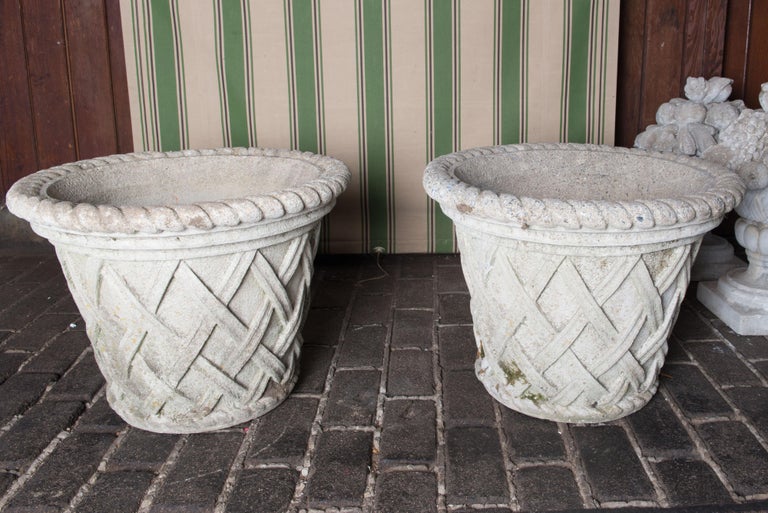 Pair of large cast stone crosshatch style planters. Rope like trim around top edge circumference. Each pot has a bottom drainage hole. They are in excellent condition.
