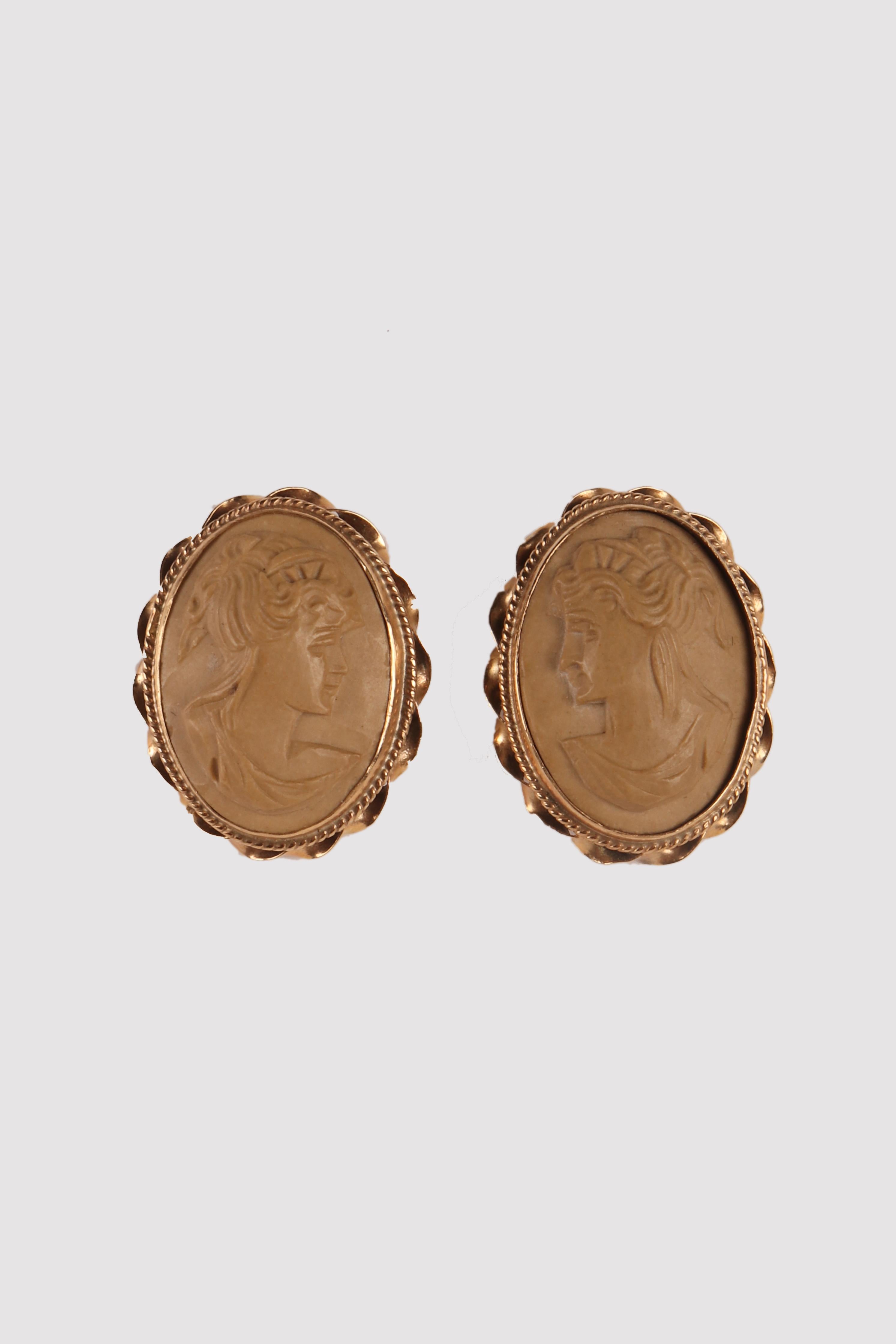 Boucles d'oreilles en or et lave. Les camées ovales, sculptés dans la lave claire, représentent deux bustes de profil de jeunes femmes aux coiffures classiques sur un fond lisse.
La monture en or 14 carats présente une lunette verticale lisse,