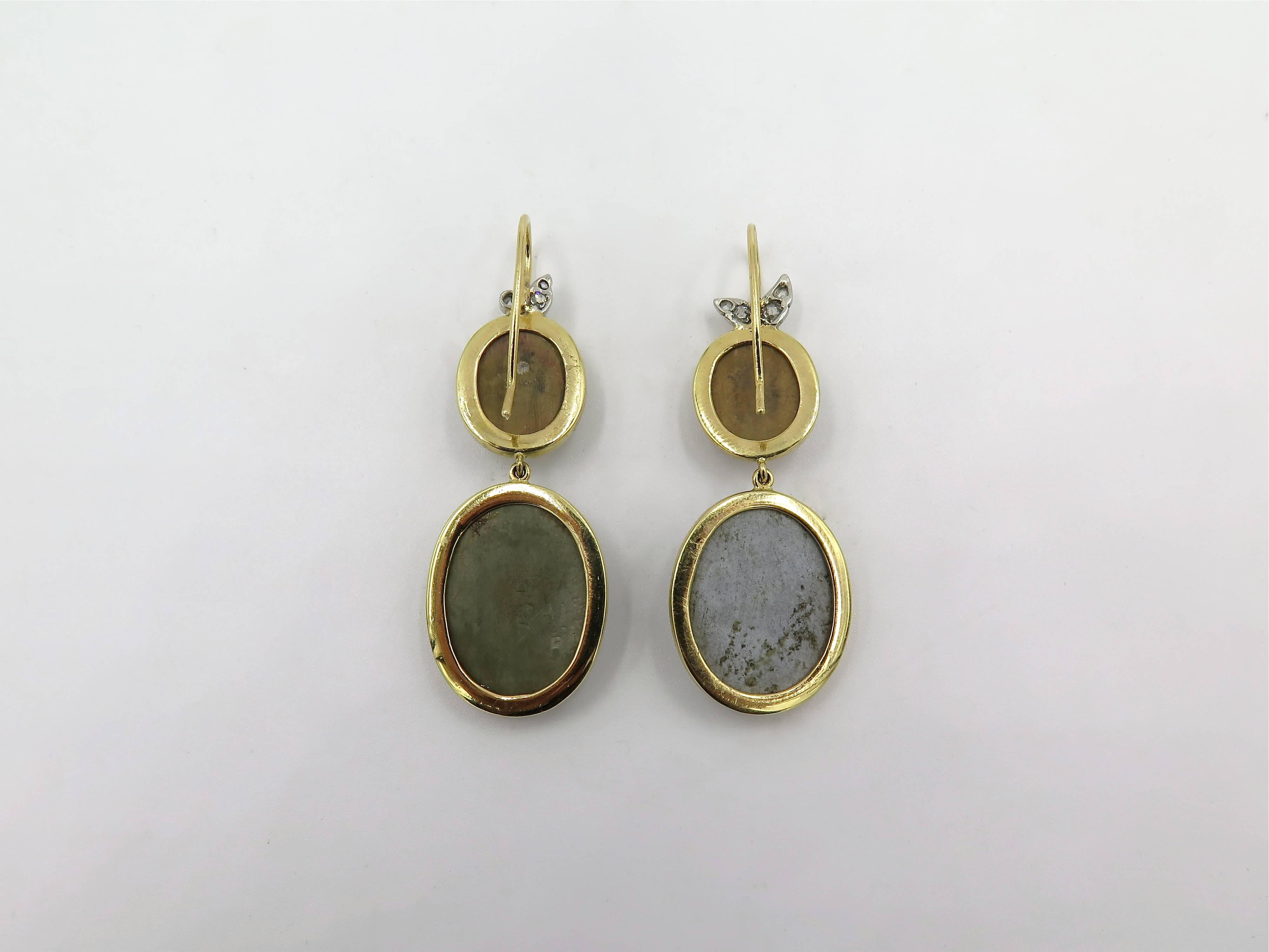 A pair of 18 karat yellow gold, platinum, diamond and bezel-set antique carved lava cameo earrings.  One earring suspends a light grey oval lava cameo depicting a bust of a woman in classical dress from a smaller light brown oval camo depicting the