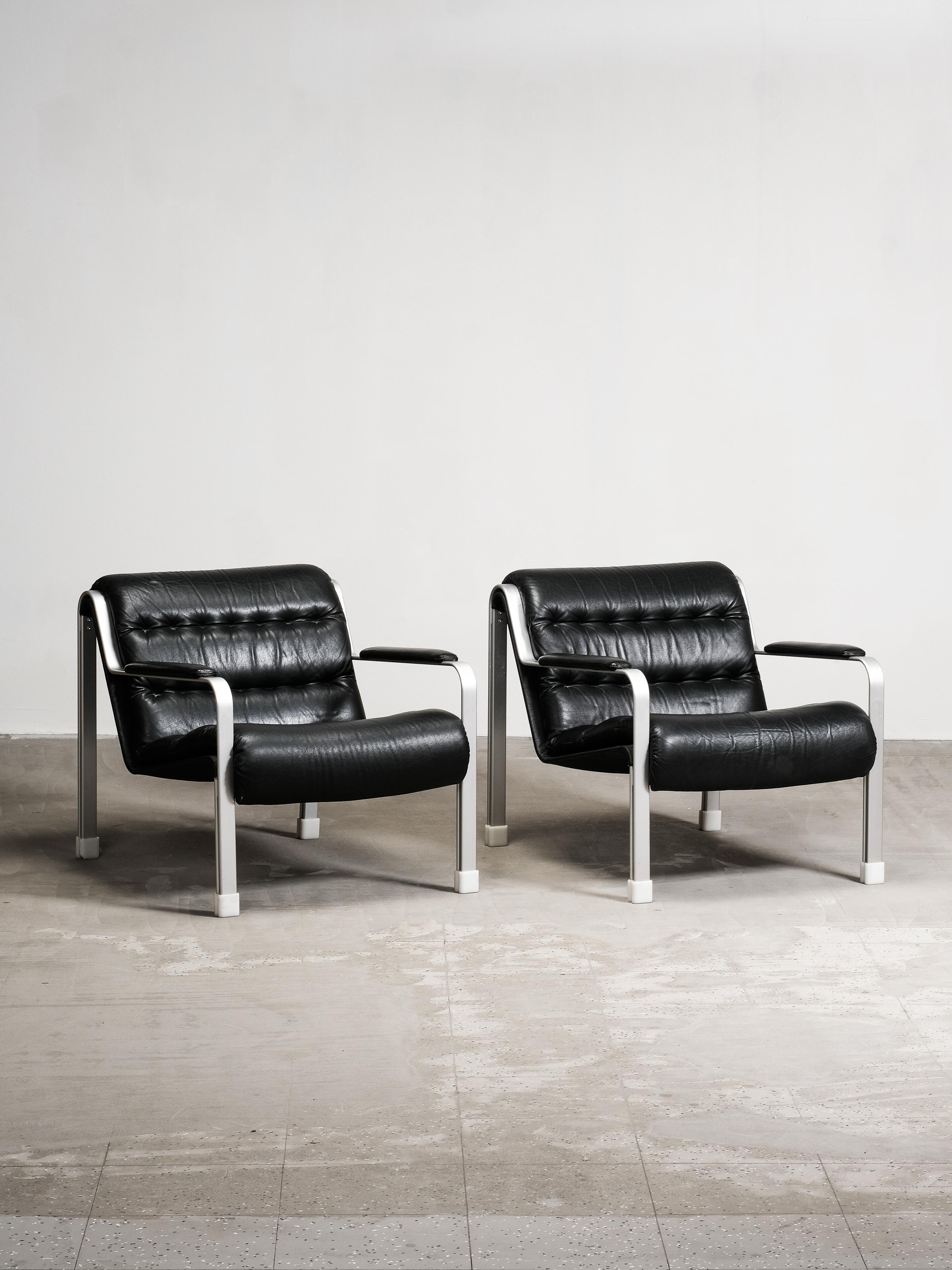 Paire de chaises de salon suédoises en cuir noir et aluminium brossé, produites dans les années 1970. Le design présente un cadre en aluminium à barre plate avec des accoudoirs légèrement incurvés, associés à des coussins profonds en cuir tufté qui