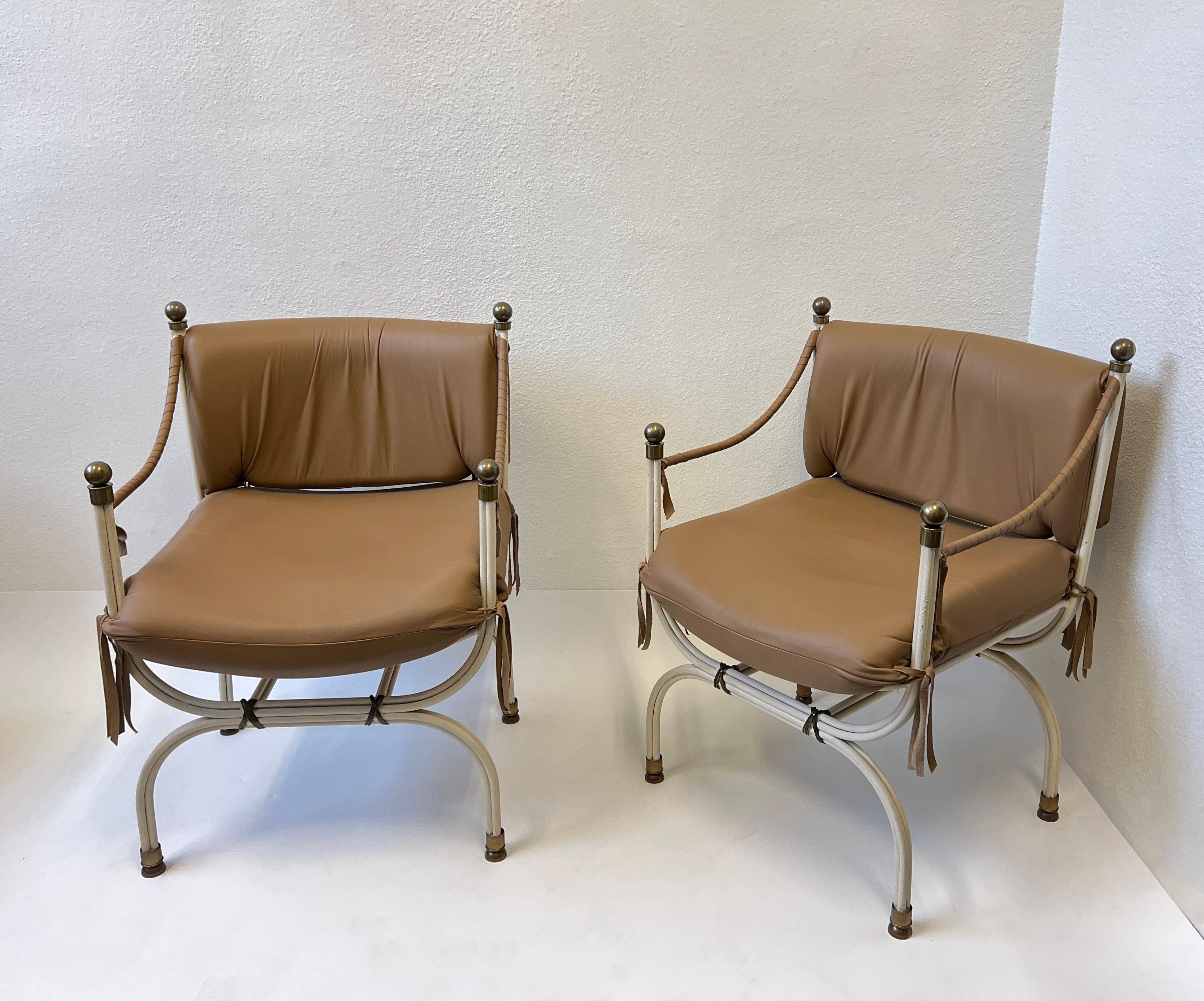 Pair of glamorous leather and aged brass campaign chairs from a Steve Chase designed estate. 
Constructed of iron with off white textures lacquered, lite mocha brown leather and aged brass details. 
In beautiful original vintage