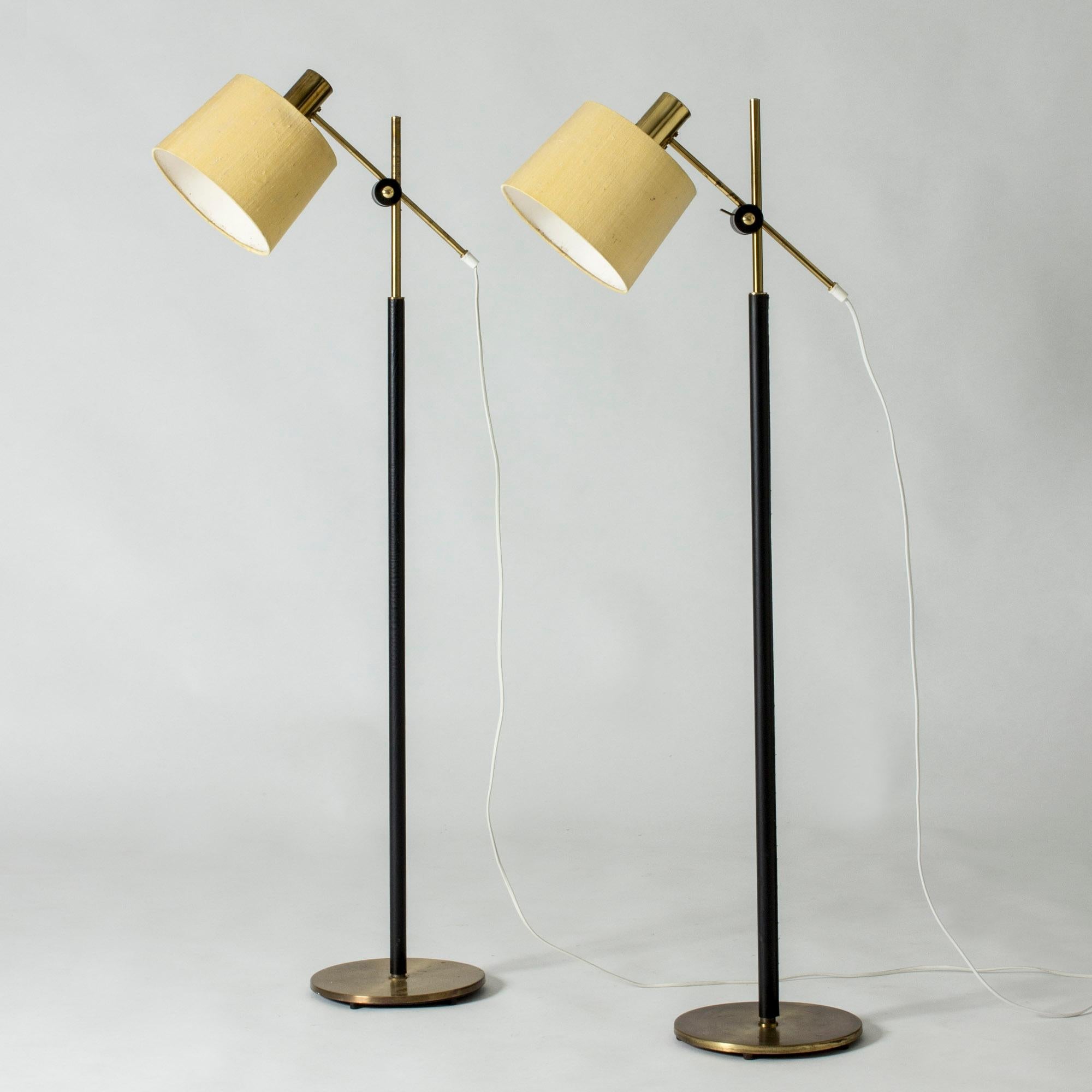 Pair of brass floor lamps from Falkenbergs Belysning. Elegant screw solution for adjusting the angle of the necks. Stems dressed with black leather. Original raw silk shades.
