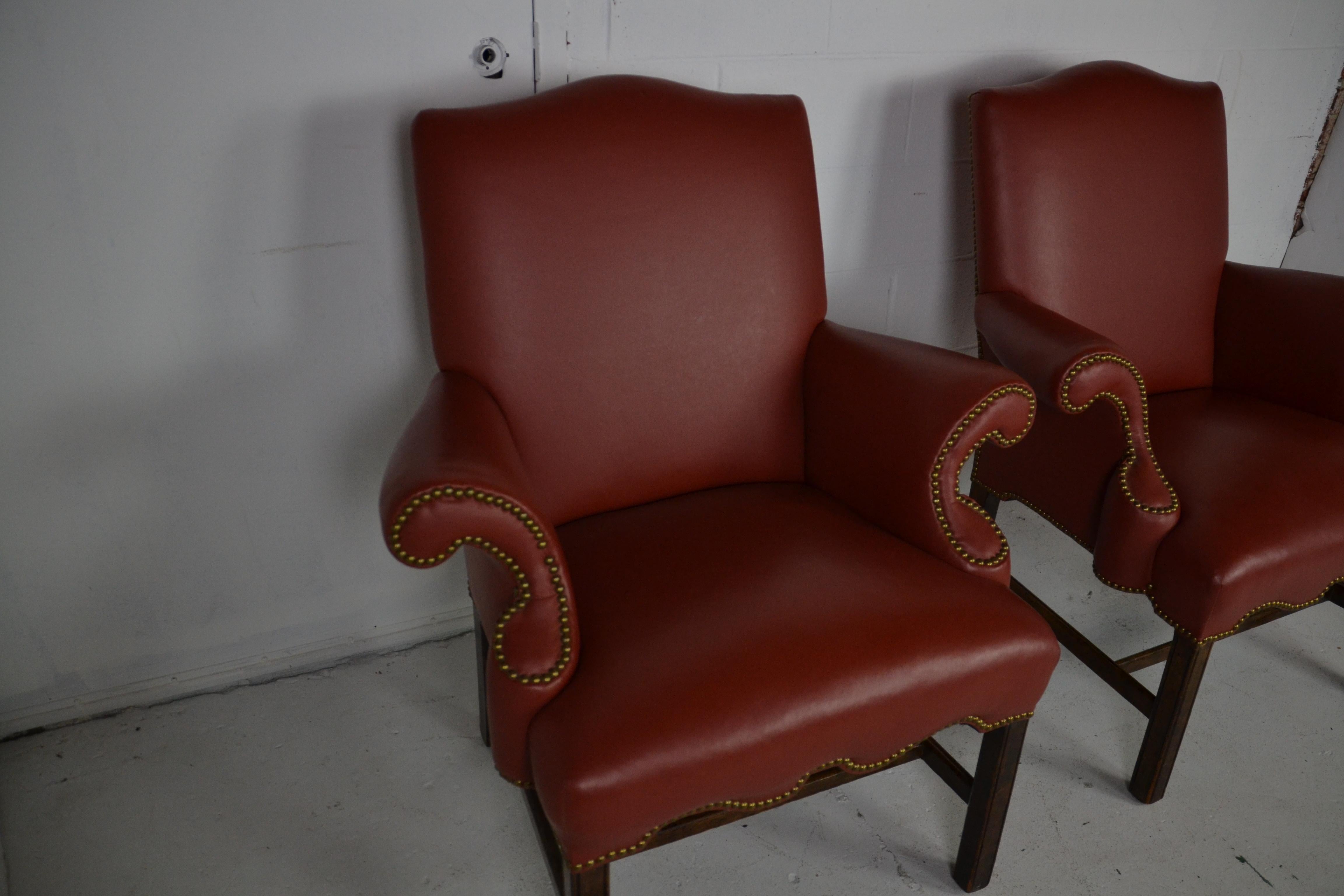 A pair of soft leather armchairs in a rust-red color. Scrolled arms and brass stud edging.