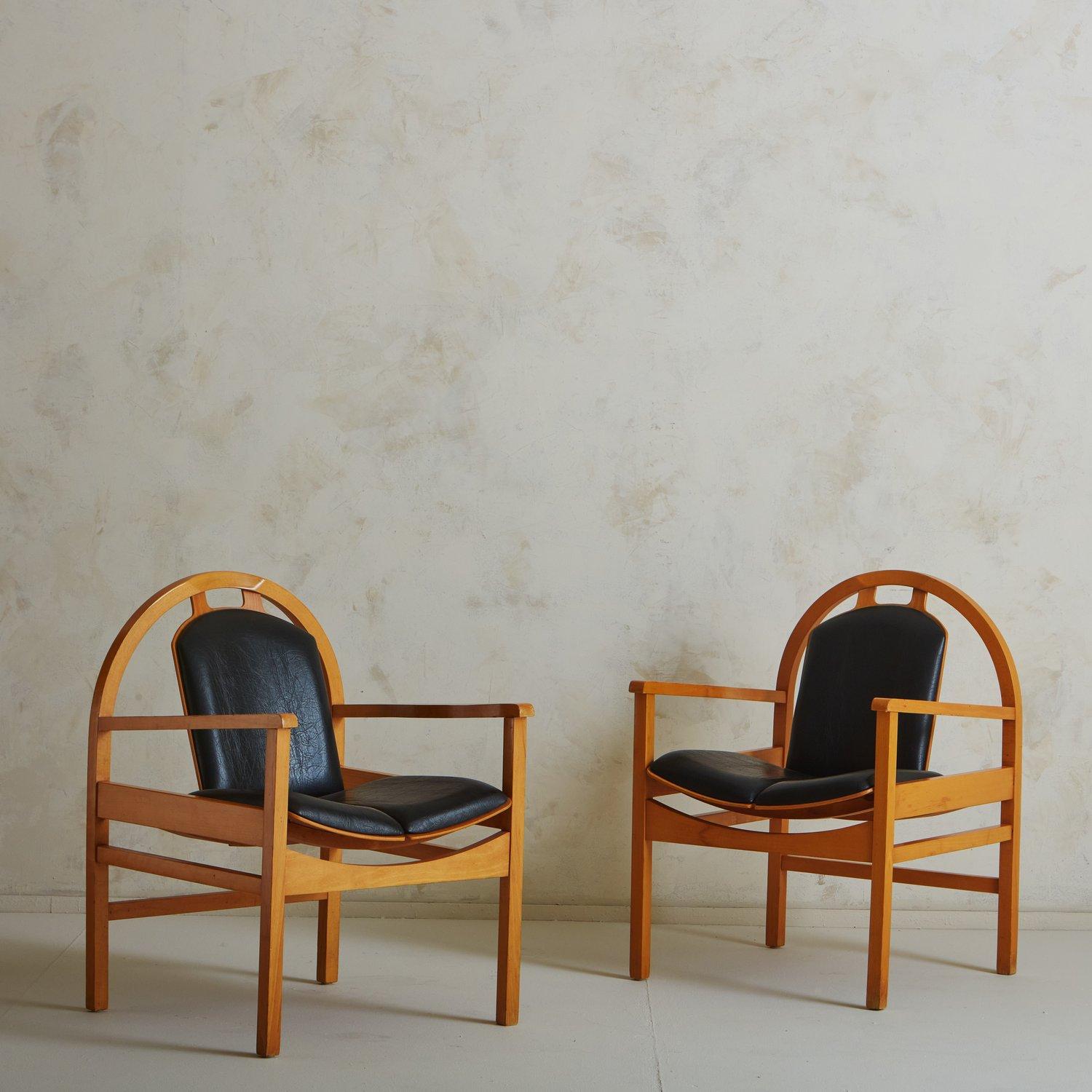 A pair of ‘Argos’ lounge chairs designed by French manufacturer Baumann in the 1970s. These chairs feature sculptural stained beechwood frames with patinated black leather seats and backs. They have rounded, angled seat backs with vertical cutout