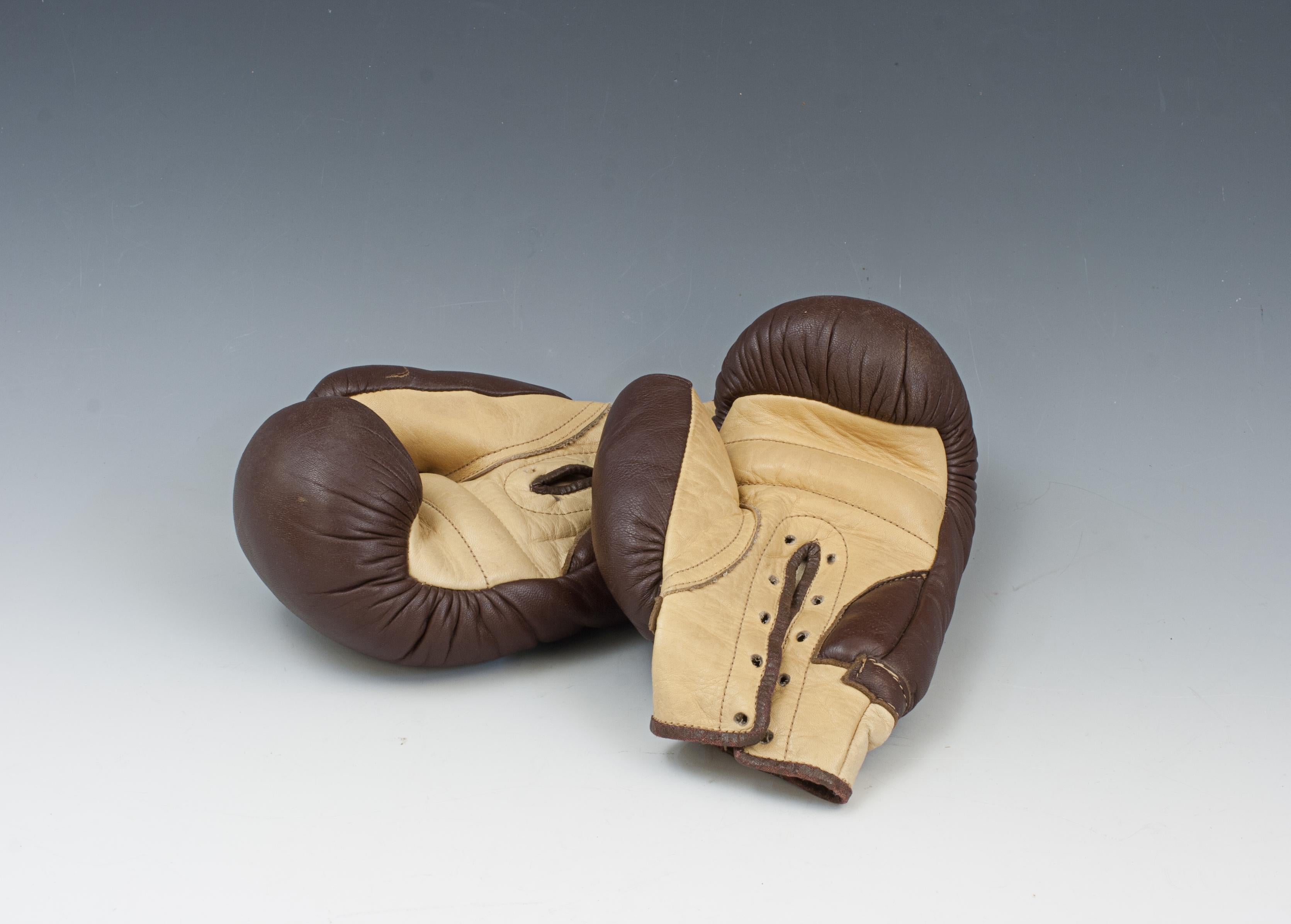 Juniors Leather Boxing Gloves.
A pair of brown and cream leather juniors boxing gloves. These gloves are with laced palms (laces missing), the leather having a nice patina about them and are in a great condition. A lovely pair of decorative vintage