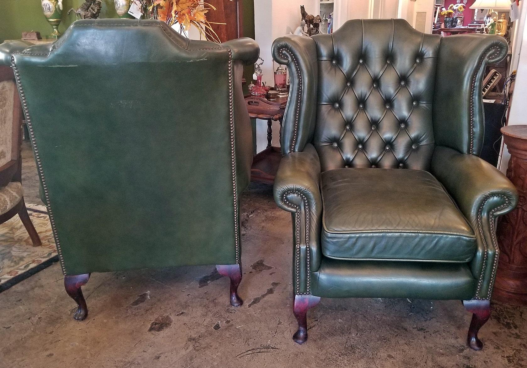 Presenting a lovely pair of mid-late 20th century reproduction armchairs.

These are a matching pair of green leather, Chesterfield Queen Ann style wing back armchairs.

Each sits on 4 mahogany footed legs in the Queen Anne Style with the button