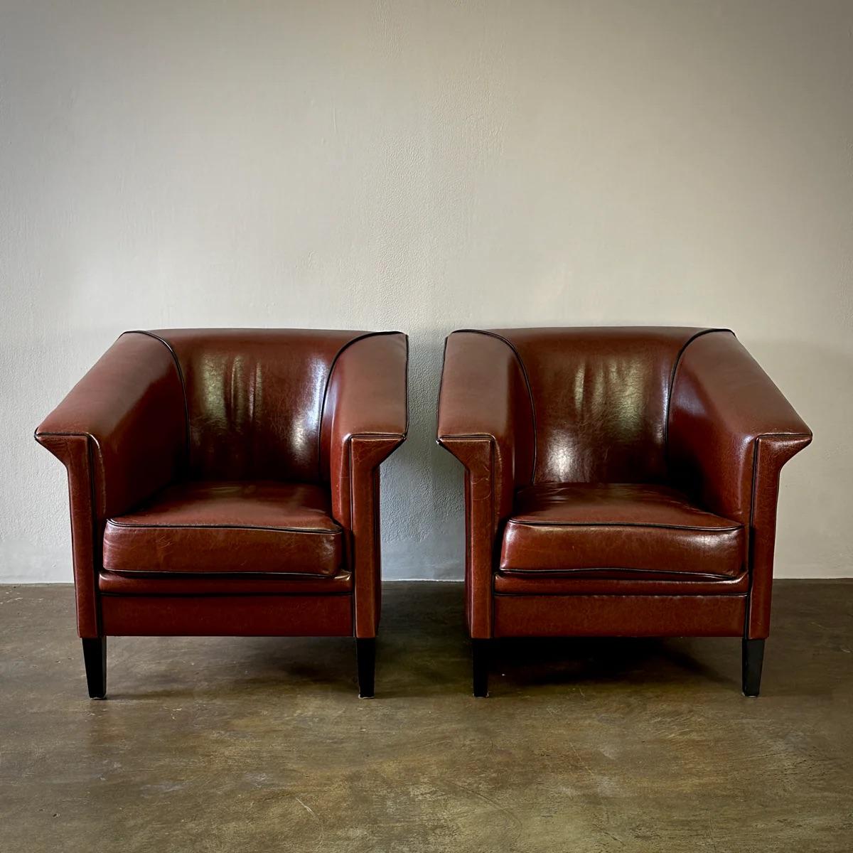 These Dutch club chairs by Bart Van Bekhovan feature high-quality conker-colored sheepskin leather, emphasizing their luxurious feel and sturdy construction. The angular lines and contrasting piping accentuate a sleek, modern aesthetic, blending