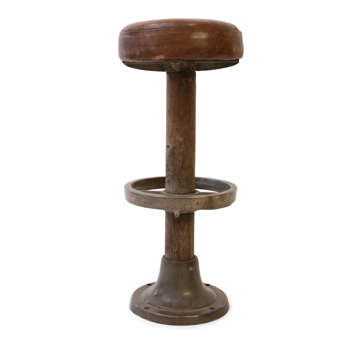 Pair of leather-covered barstools, or counter stools, (circa 1910-1940) originally from an ocean liner (large passenger ship). Seats covered in nice, old leather atop wood pedestals. Bronze-on-nickel circular foot rests and bases are both solid.