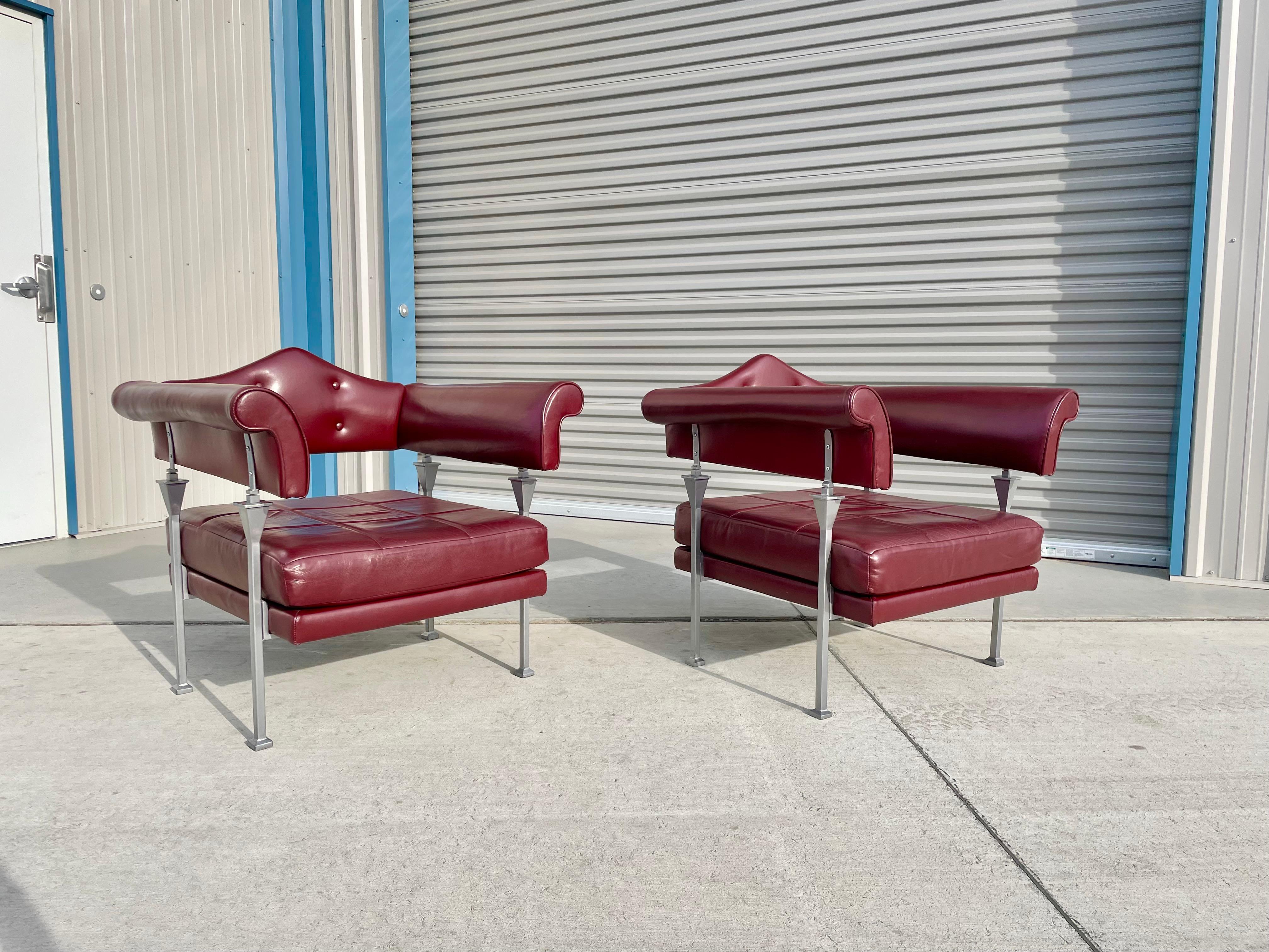 Mid-century modern pair of leather armchairs was designed by Luca Scacchetti and manufactured by Poltrona Frau in Italy circa the 1990s. These beautiful lounge chairs feature red leather tufted backrests with a unique metal base, making them the