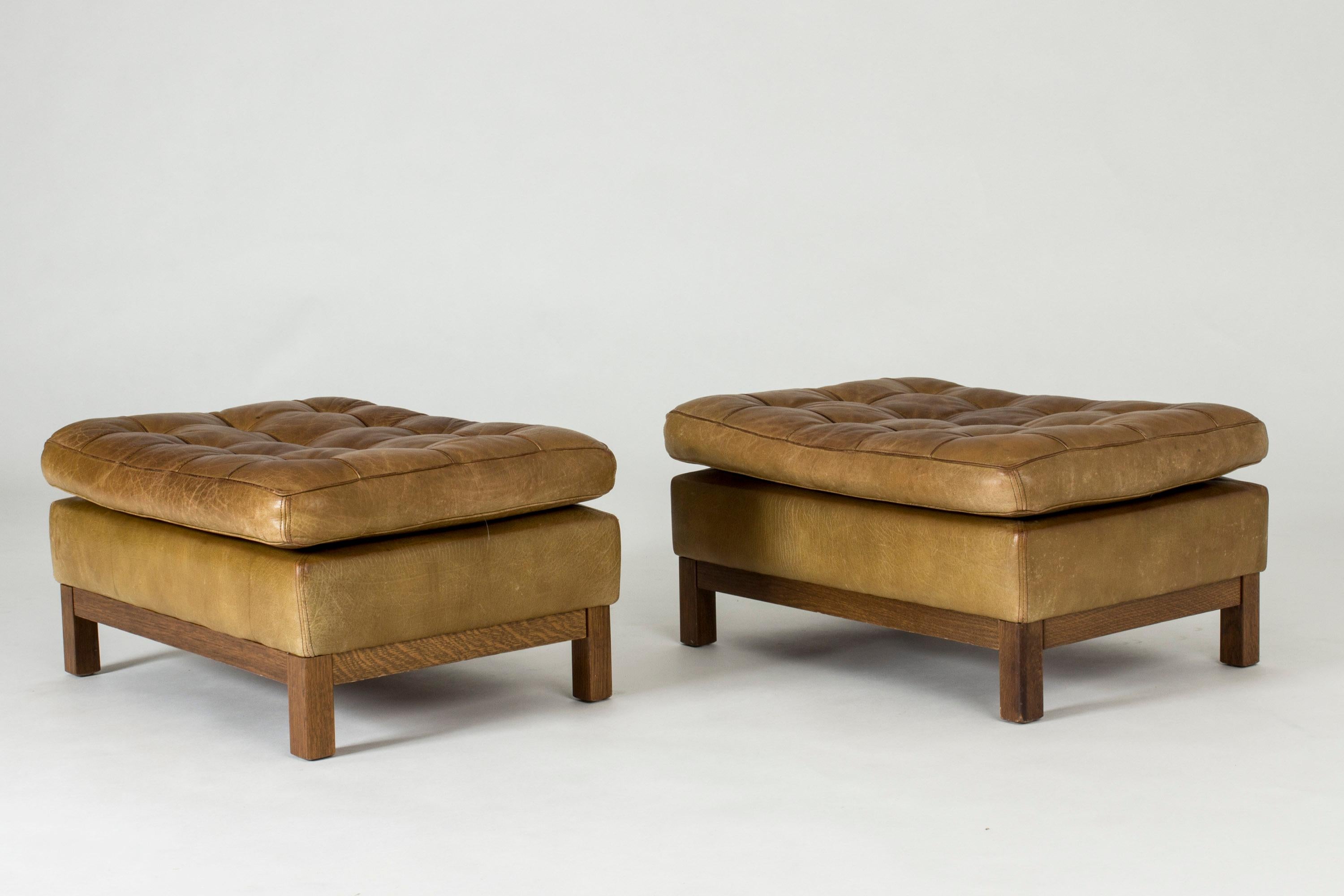 Pair of cool leather ottomans or footstools by Arne Norell, upholstered in tan leather. Decorative buttons and checkered seam pattern.