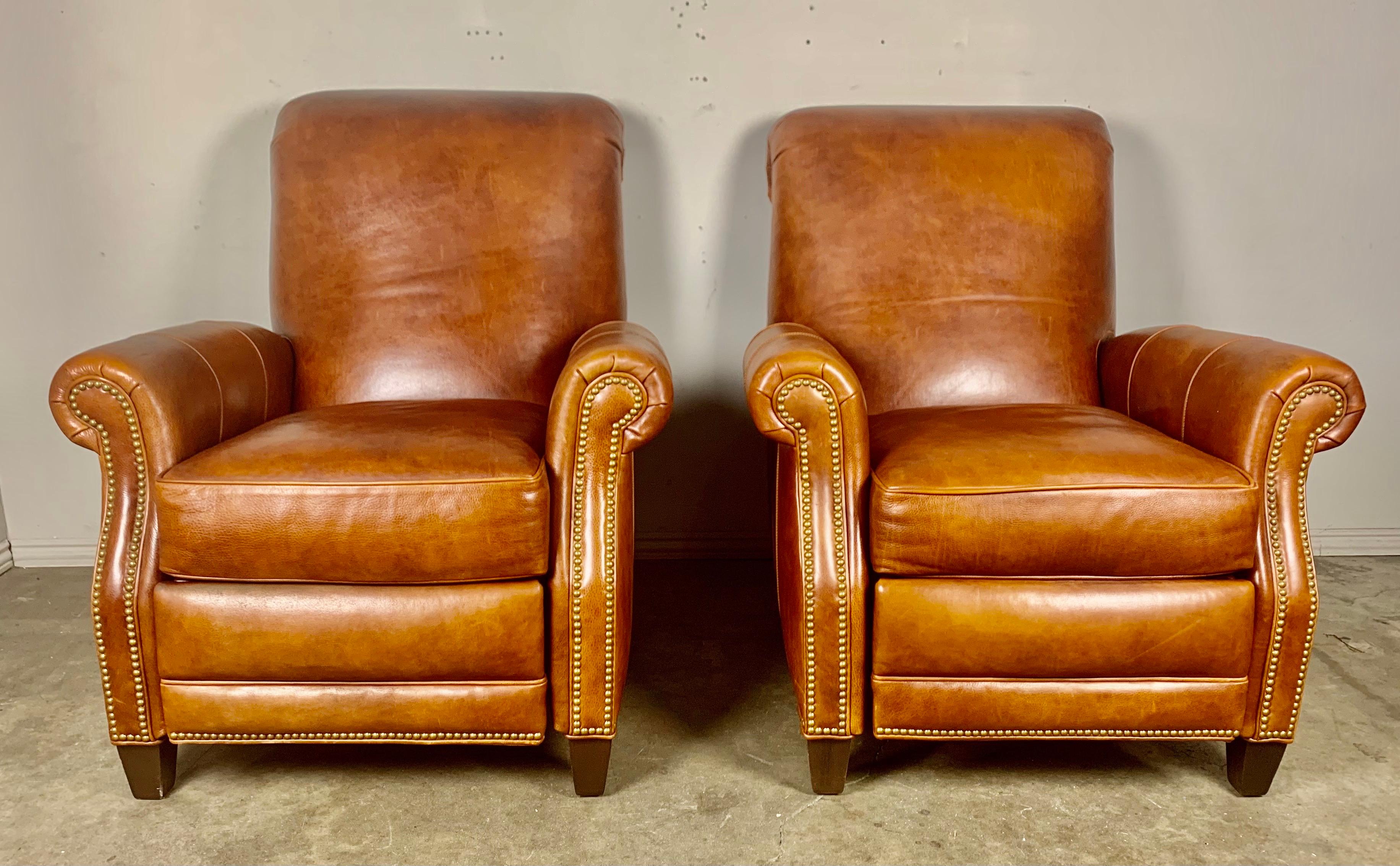 Pair of leather recliner armchairs. This pair of tobacco colored leather armchairs have a reclining mechanism as depicted in photos. This elegant pair of leather armchairs are detailed with nail heads. The armchairs stand on four wood tapered legs