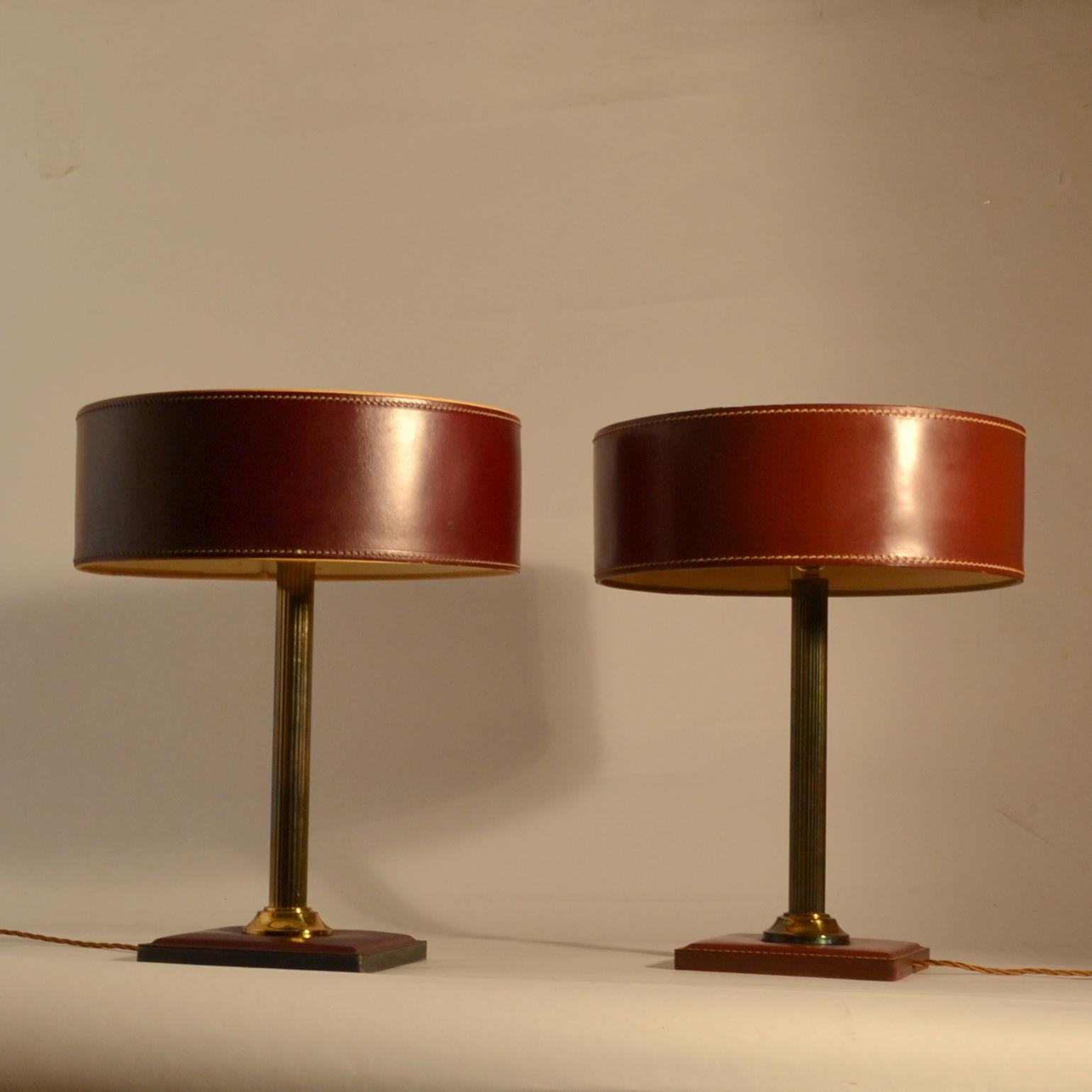 Red-brown leather table lamps with a cylinder shade and square base with detailed contrasting stitching standing on a brass stem.
Variations on this model available.