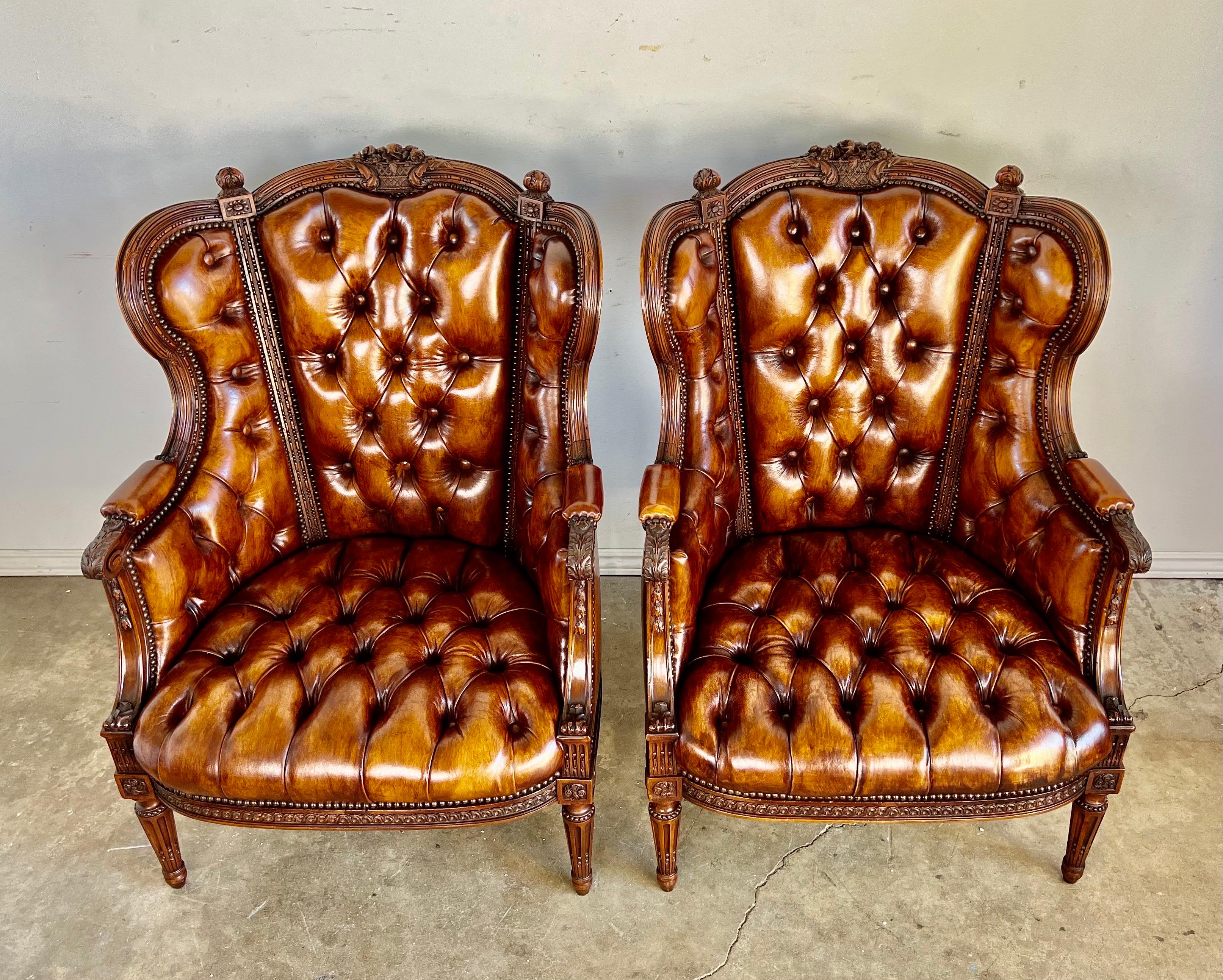 Pair of early 20th century wingback French leather tufted armchairs. The chairs stand on four straight fluted legs. They are upholster in tufted caramel colored leather with nailhead trim detail. These armchairs were finely carved with beautiful