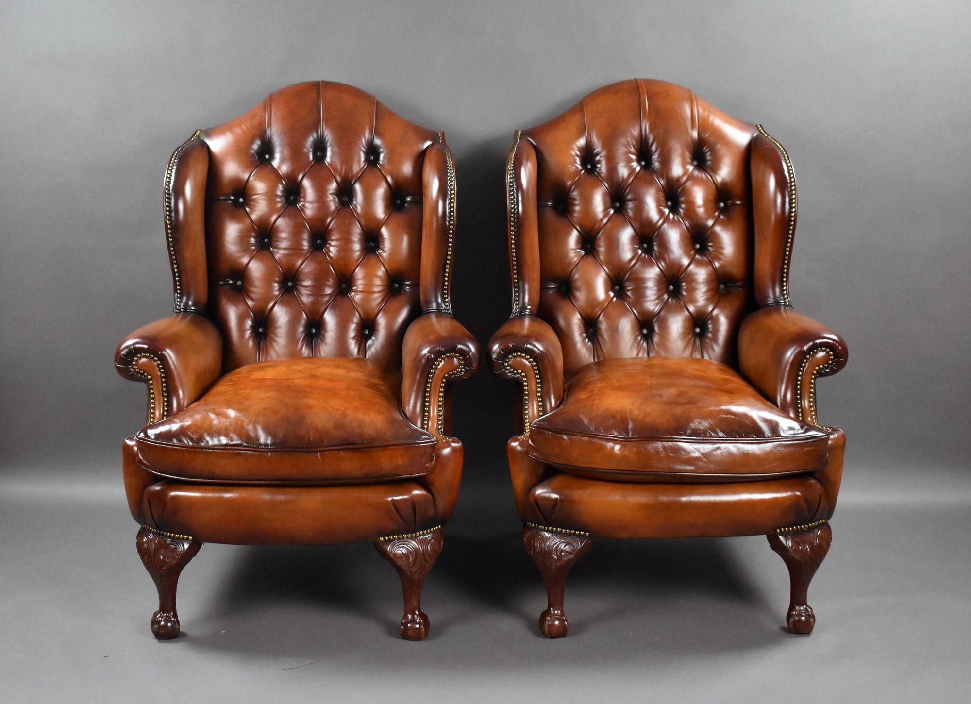 Il s'agit d'une paire de fauteuils à oreilles en cuir de très bonne qualité, avec des dossiers en forme et profondément boutonnés, au-dessus d'un coussin rembourré de plumes, reposant sur d'élégants pieds griffes et boules sculptés. Chaque fauteuil