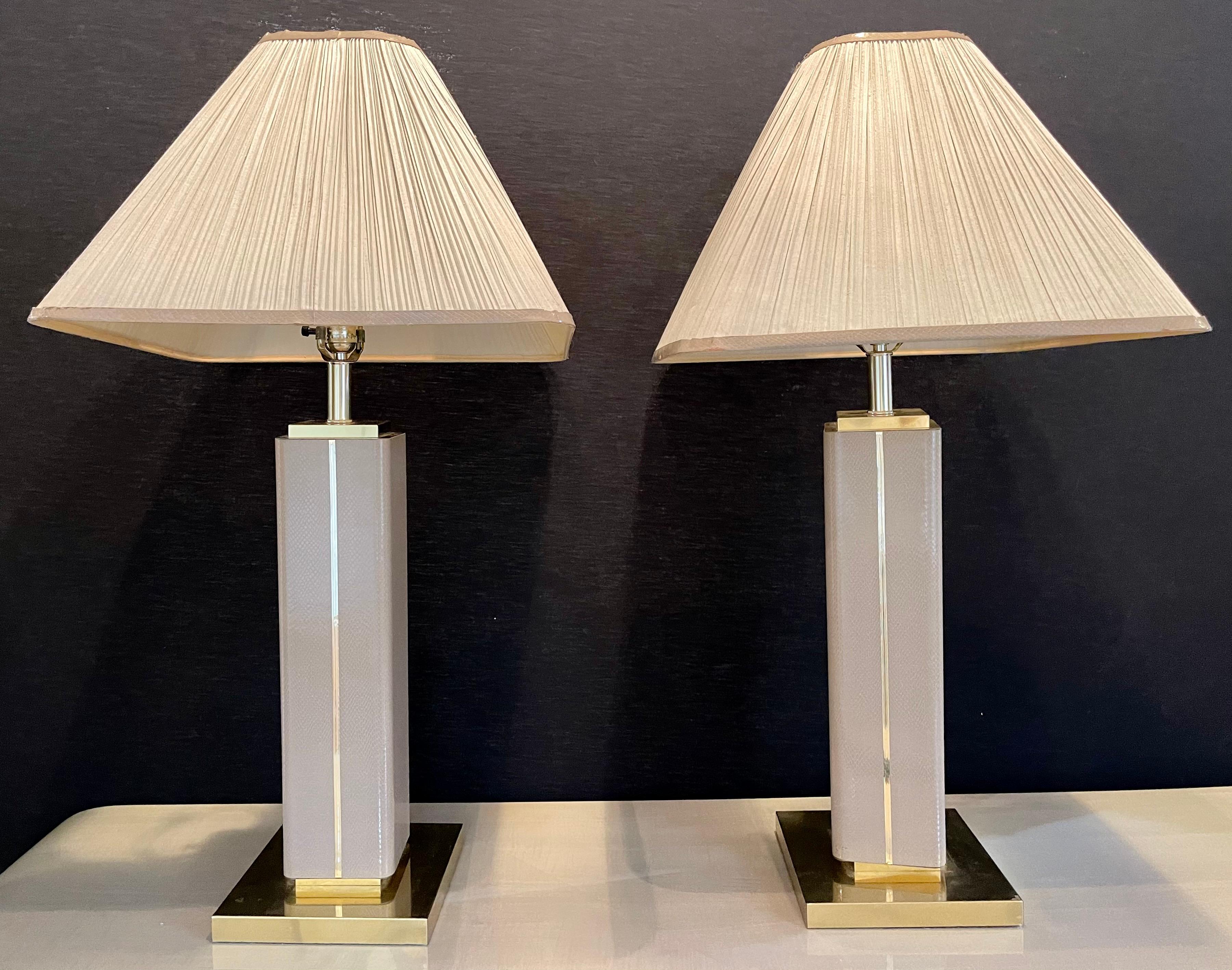 Pair of leather wrapped modern table lamps with custom shades. These table lamps are simply spectacular. Sleek and stylish as one would expect from this highly acclaimed designer. The pair finely wrapped sit on gilt metal bases with matching pole