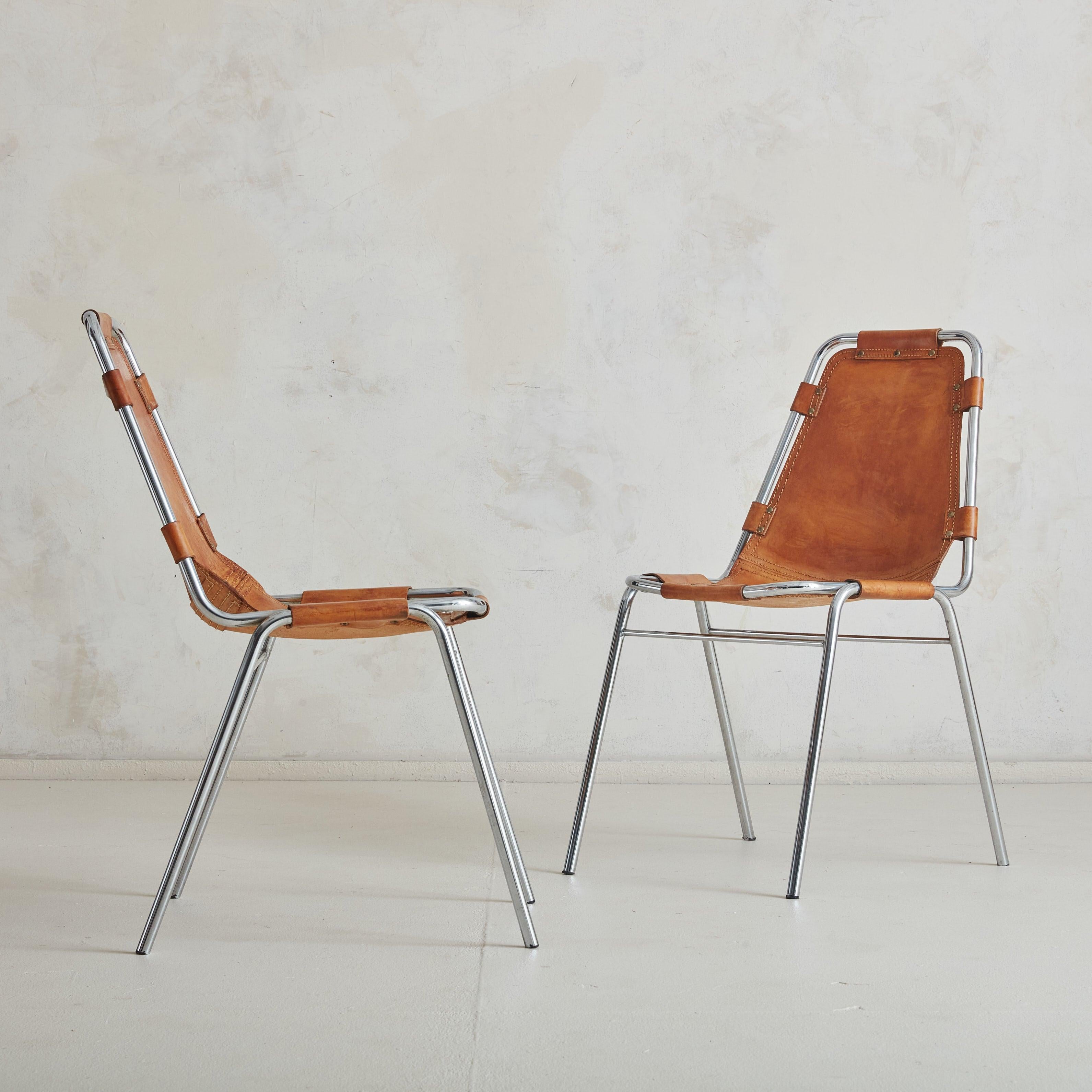 Paire de chaises Les Arcs du milieu du siècle, attribuées à Charlotte Perriand. Ces chaises sont dotées d'une structure tubulaire chromée et d'une assise et d'un dossier en cuir cognac surpiqué, qui se fixent à la structure à l'aide de sangles en