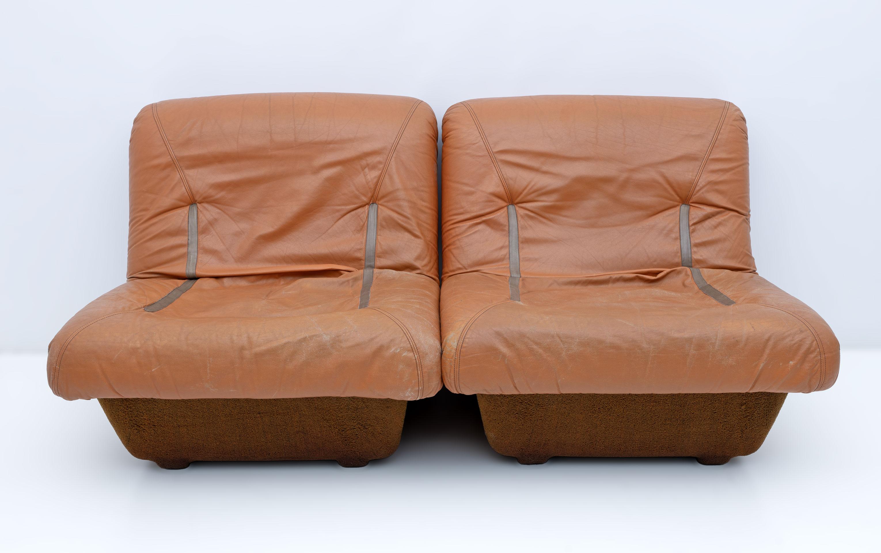 Canapé modulable composé de 2 fauteuils en cuir véritable déhoussable avec structure en fibre de verre recouverte de tissu technique de type bouclé marron. Le cuir apparaît, comme sur la photo, usé par le temps et l'usage mais très résistant, souple