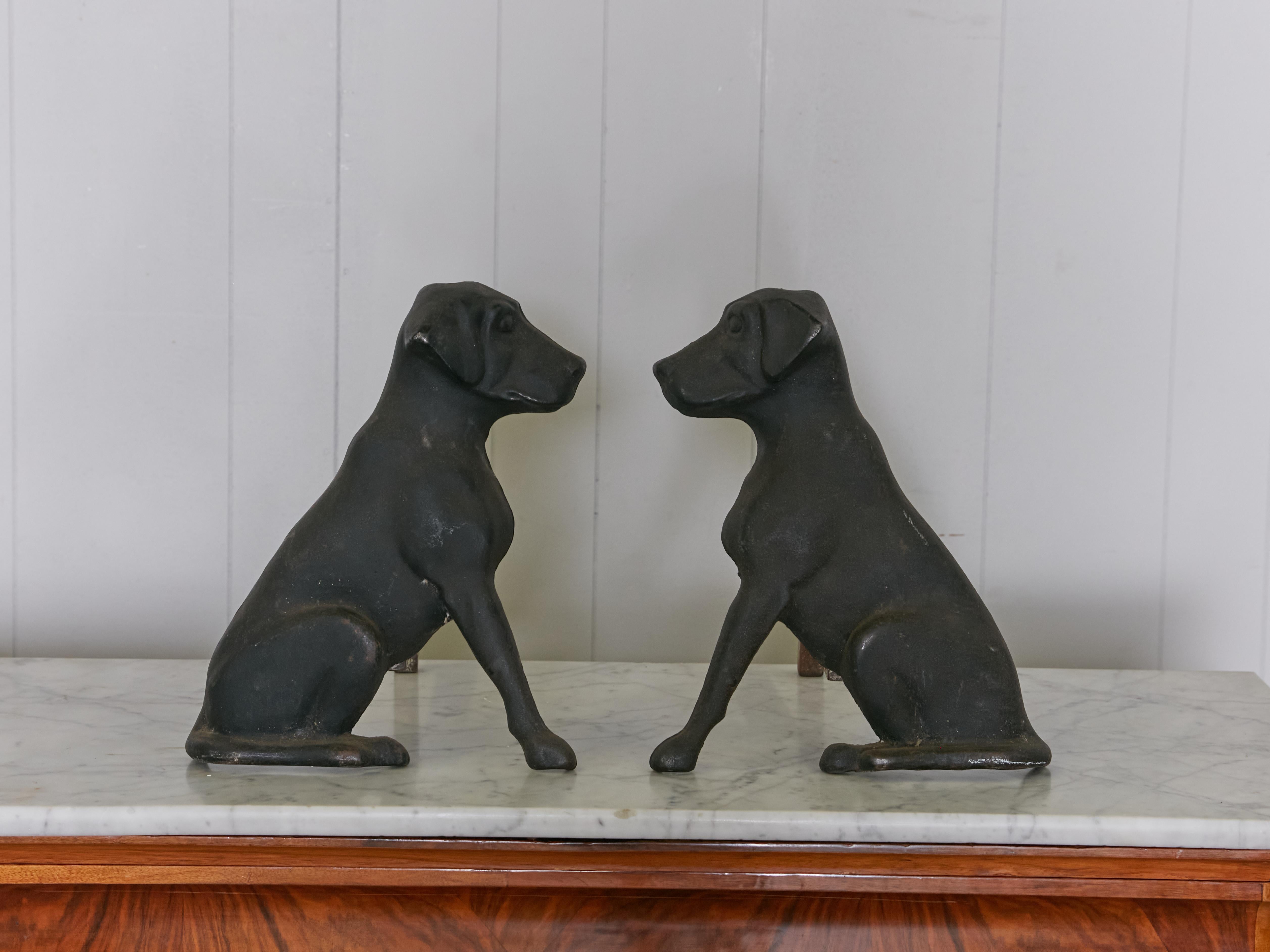 A pair of vintage American cast iron labrador dogs andirons from the mid 20th century, with black patina, stamped Liberty Foundry St Louis. Made in Saint Louis, MO during the Midcentury period, this pair of cast iron andirons comes from the Liberty