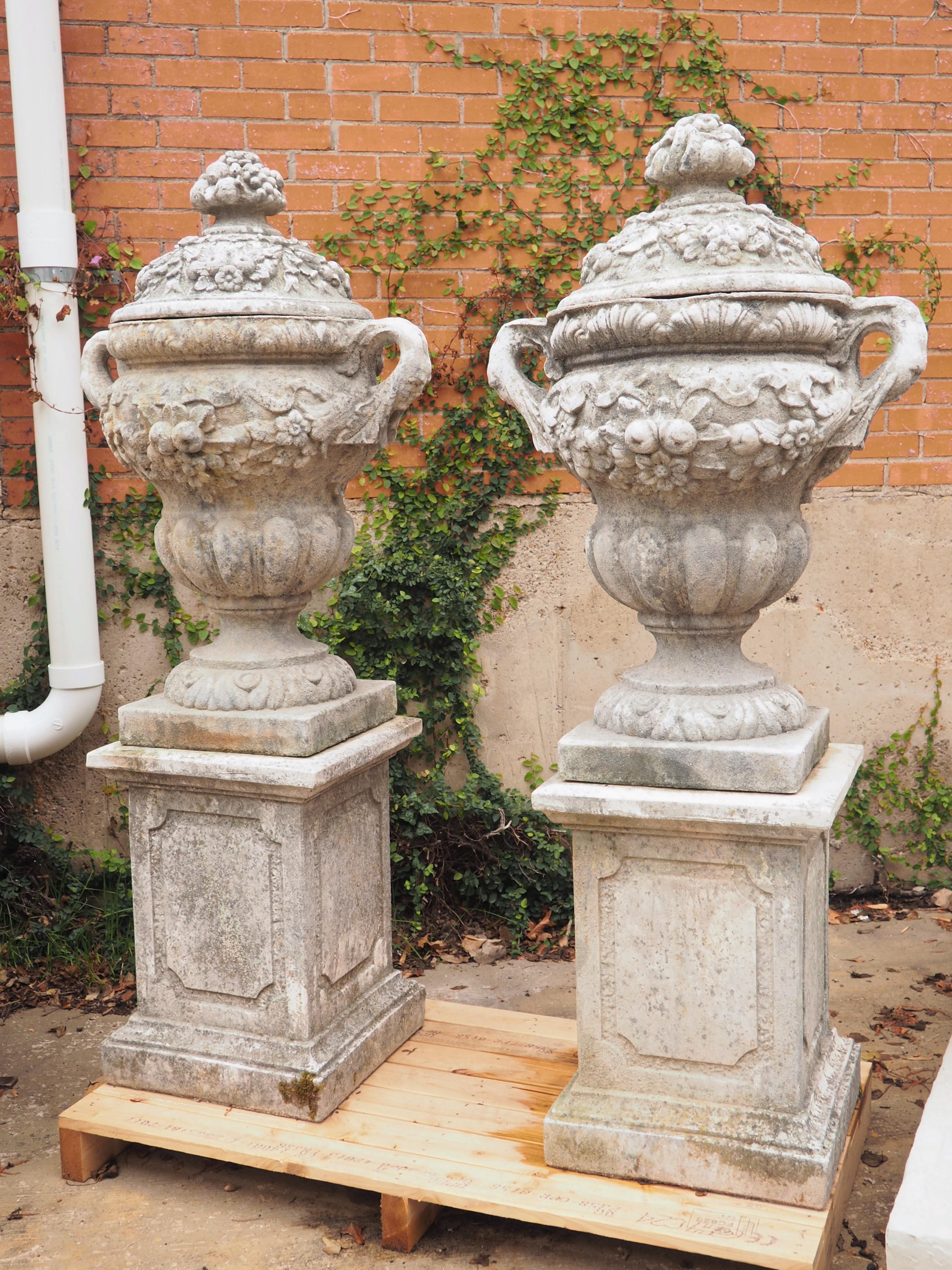 These regal French lidded garden vases rest on a classical, one-piece plinth with a molded entablature. As they have been resting in Normandy for the past 10 years, they have developed a natural gray/brown patina with traces of moss. The lids