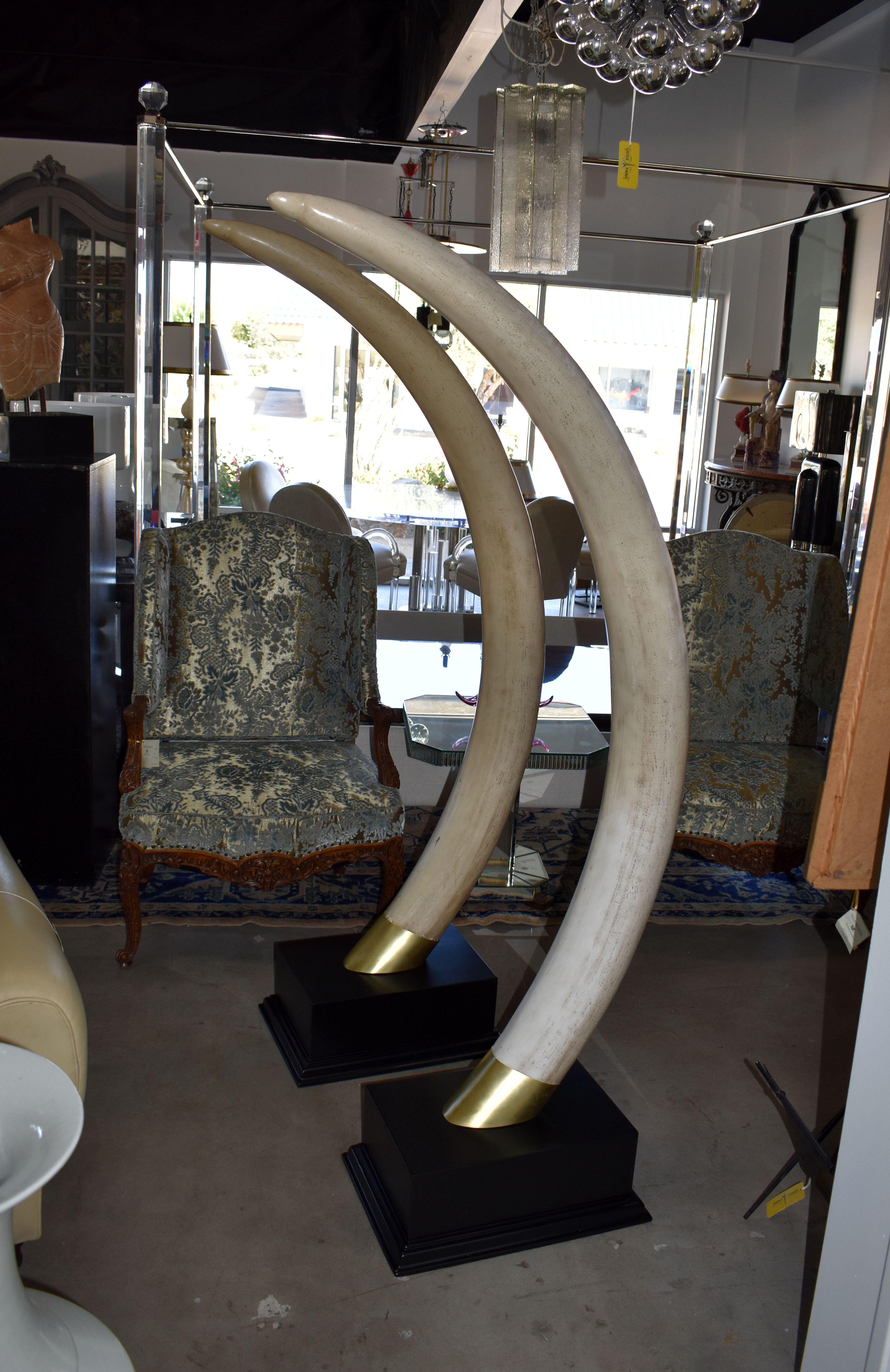 Pair of 1970s resin faux elephant tusks with black lacquered painted finish base and brass detail.

Measurement:
Depth middle of tusk 31 inches.
 