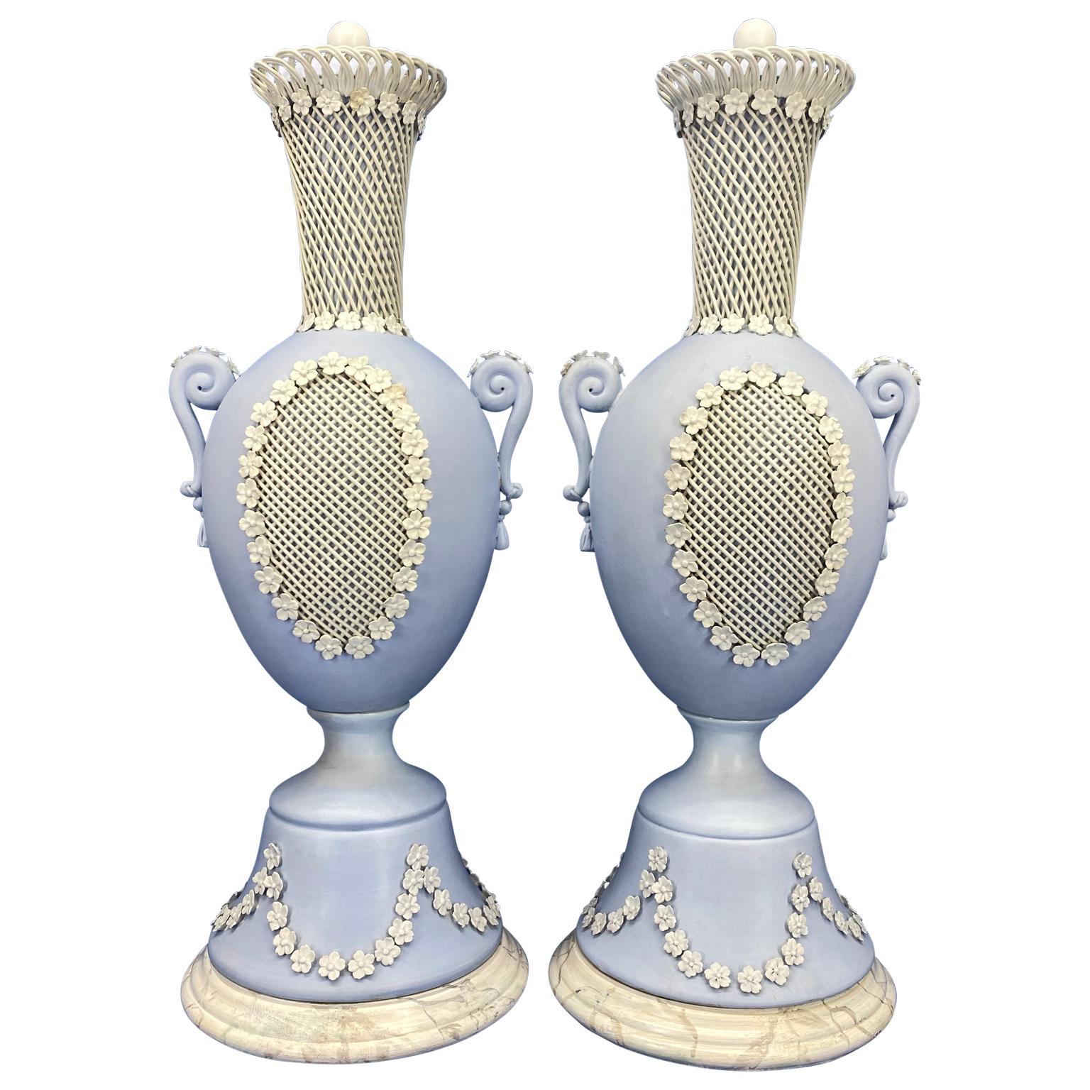 Pair of Wedgwood blue Jasperware urns or ornamental vases with covers.

Each urn with applied white floral design, including small leaves, bell flowers and relief with floral festoons. The urns are secured on two later faux marble wood bases. A