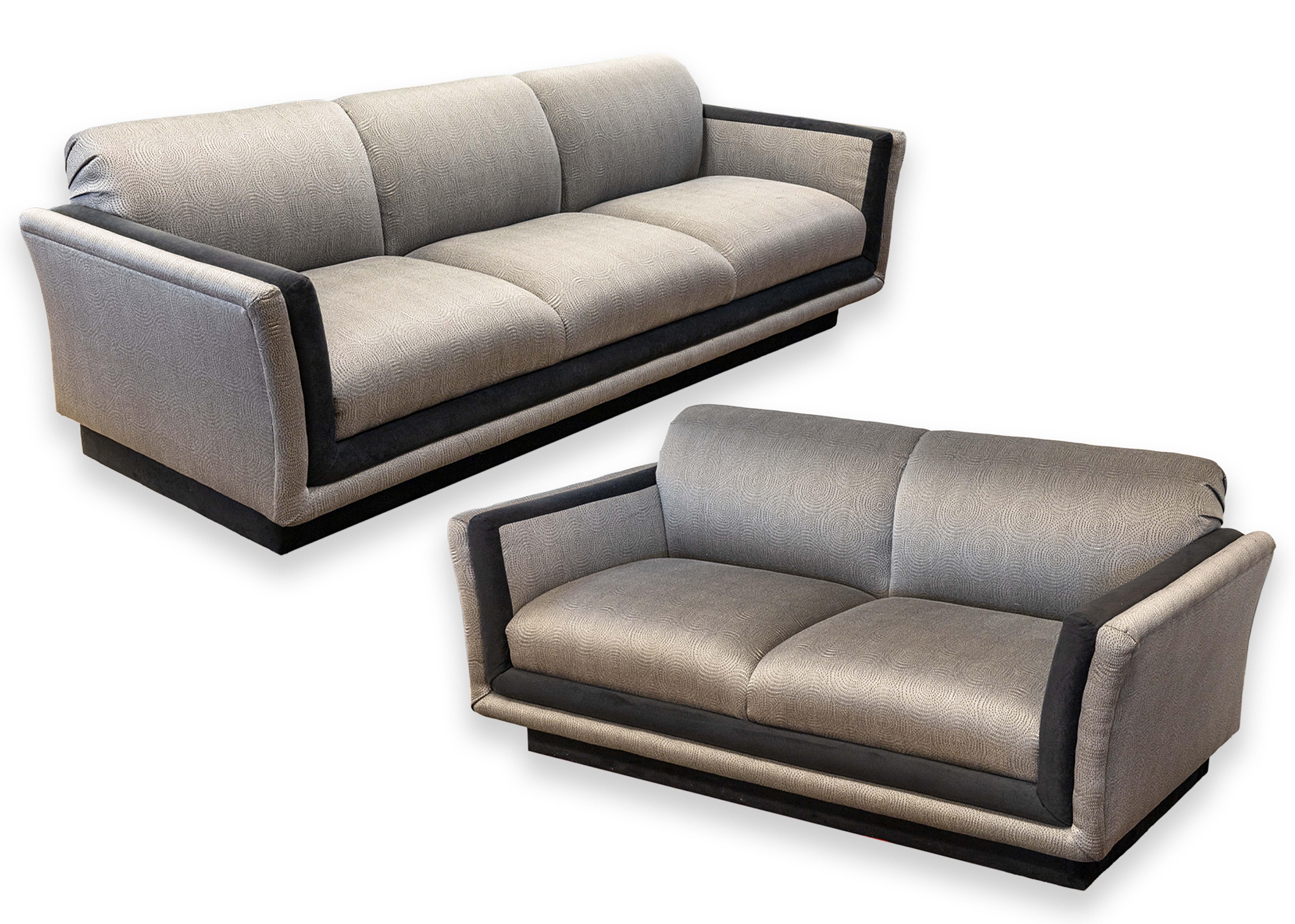 A pair of Ligne Roset matching sofa and loveseat. This awesome pair of living room piece feature a matching modern design. They are both dressed in a gray and black upholstery. The gray fabric that covers the majority of both pieces features a