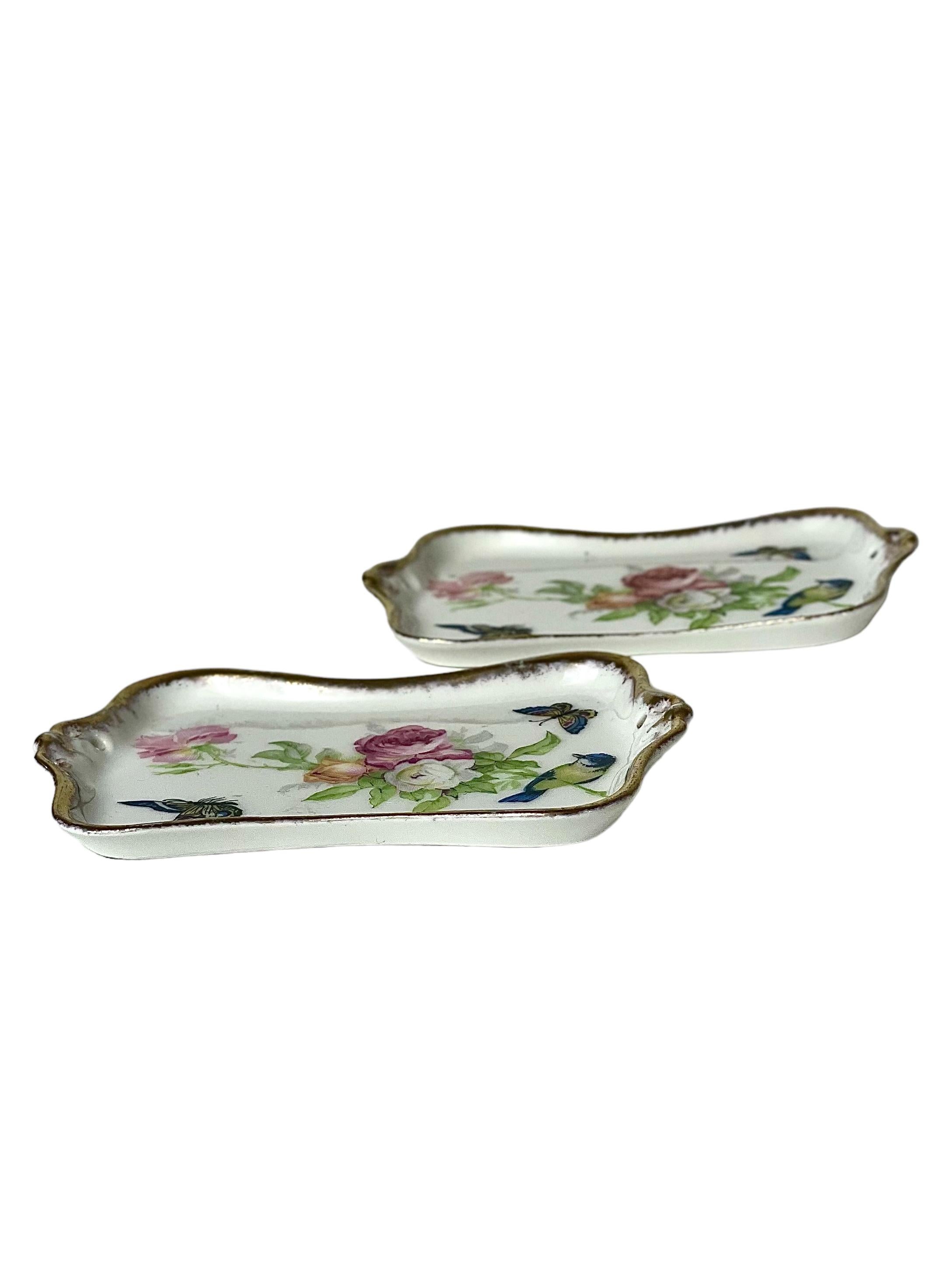 A charming pair of trinket dishes in delicate Limoges porcelain, beautifully painted with a spray of wild roses, butterflies and a blue tit, and edged in gilt around their rims. Known as 'vide poches' (emptying pockets) in French, these useful