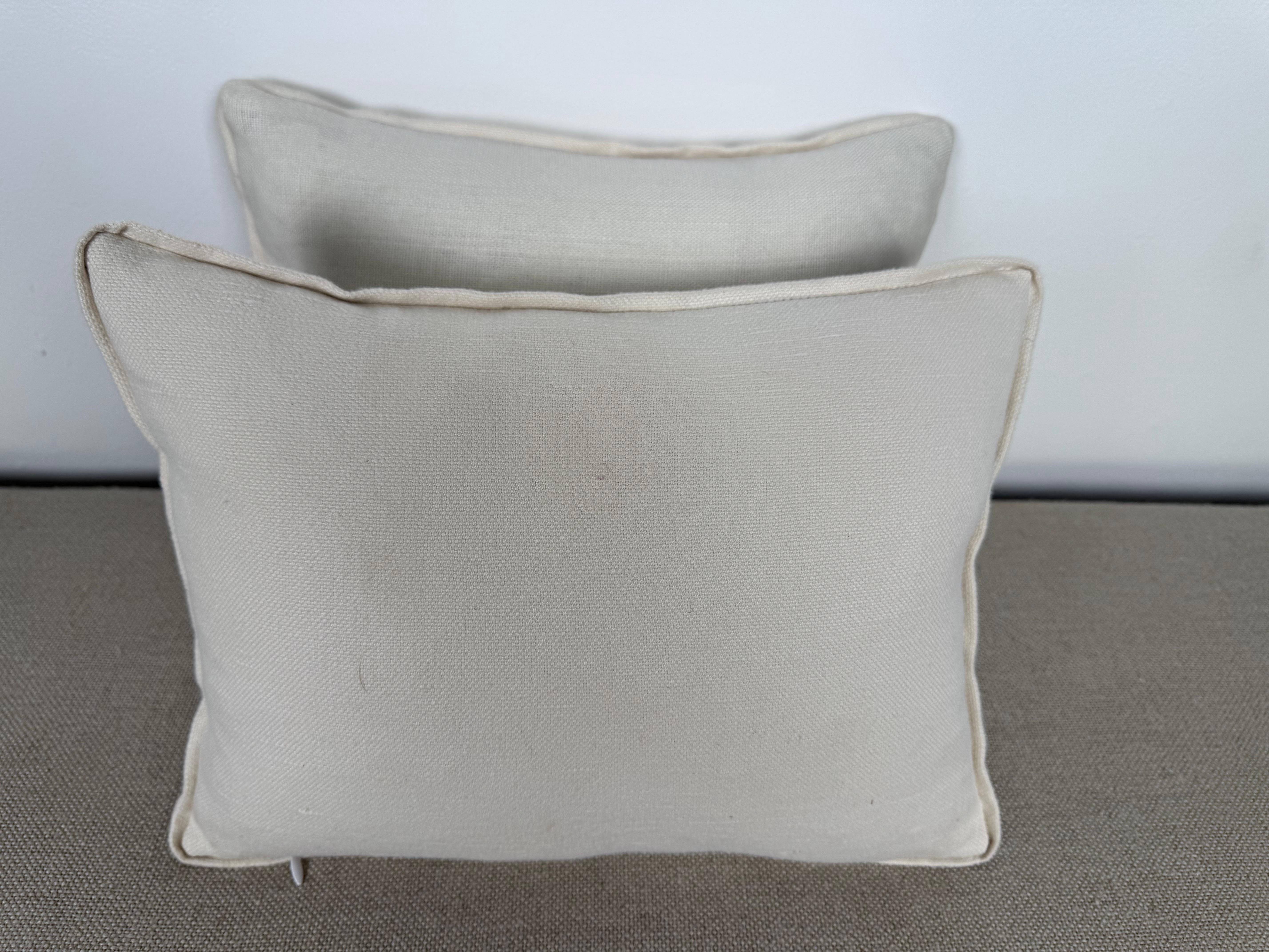 Questi piccoli cuscini decorativi sono realizzati in fresco lino bianco e presentano squisiti dettagli ricamati da Embroidery Palace. La parte anteriore è ornata da un elegante motivo a vite che scorre, con foglie stilizzate in una fresca tonalità