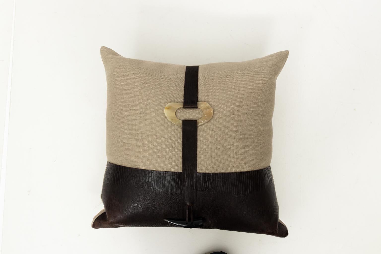 Pair of beige and brown throw pillows with embossed faux leather and faux bone trim. Feather and down inserts.