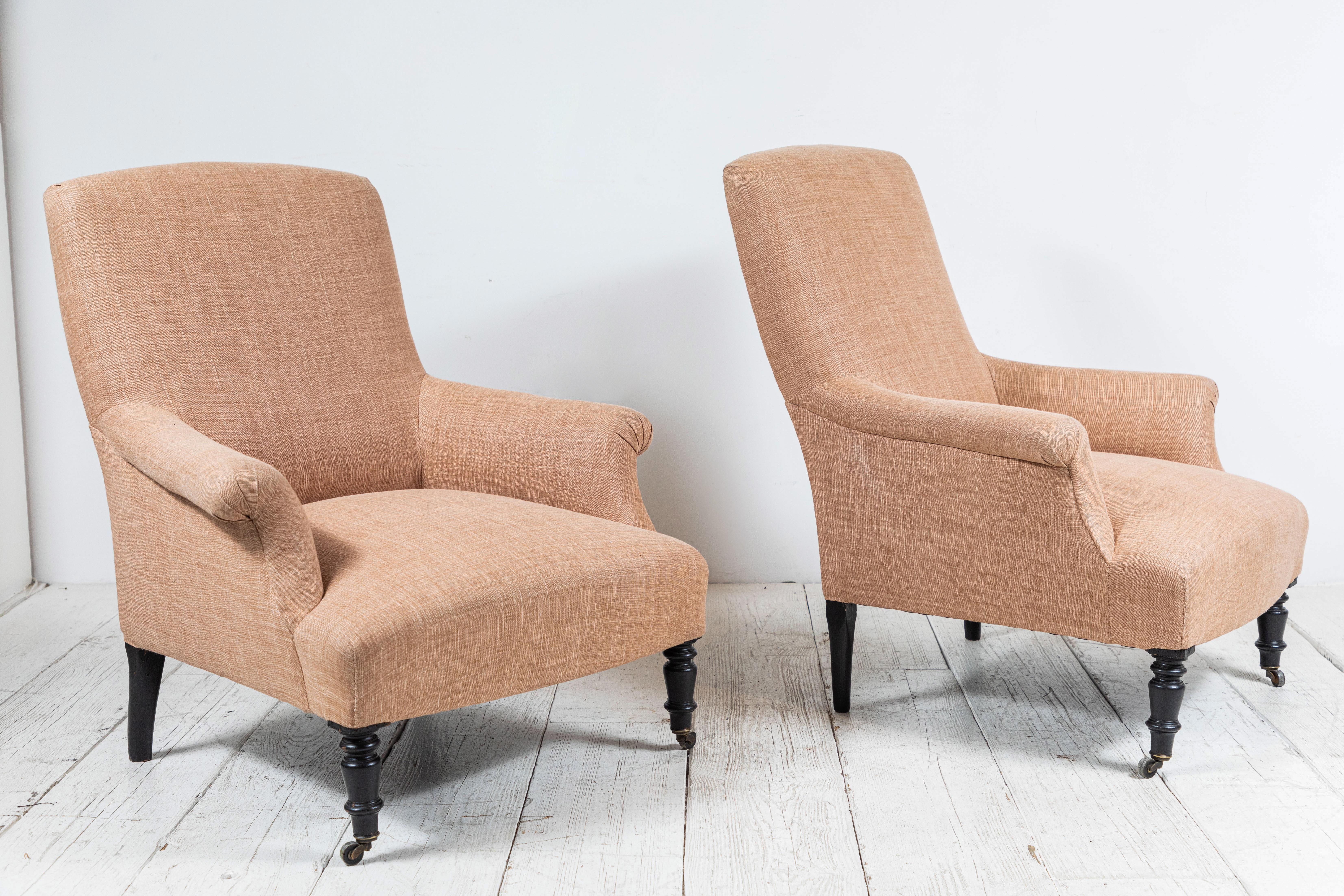 Pair of French club chairs upholstered in rose colored Linen. Club Chairs are offered with original turned legs on casters.