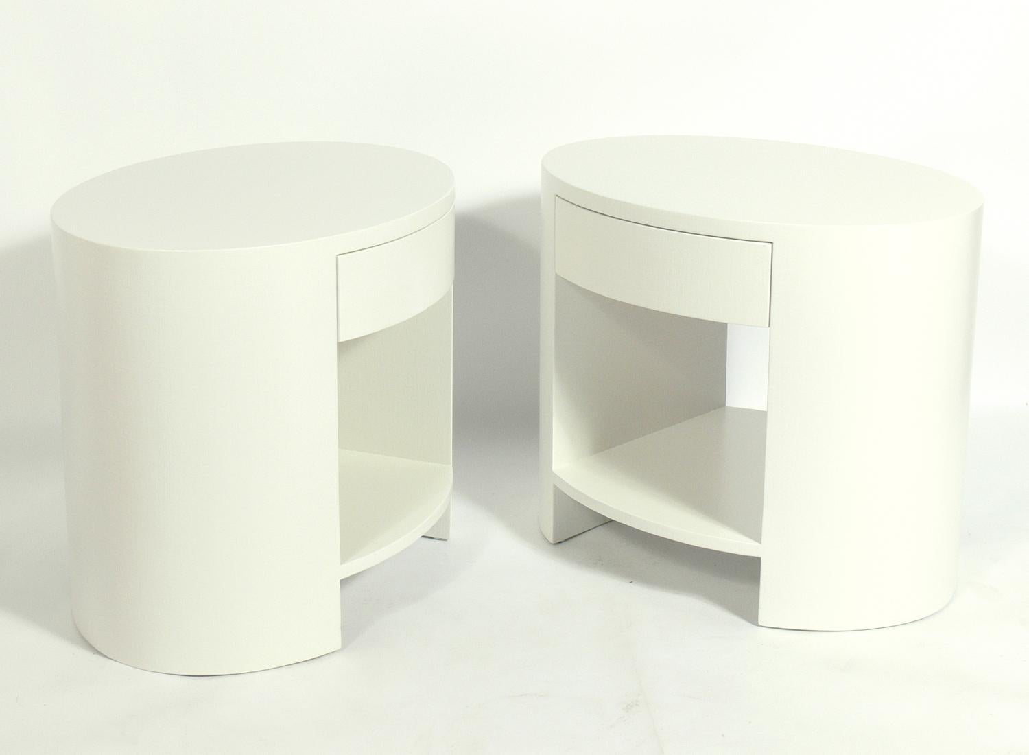 Pair of linen wrapped oval night stands, in the manner of Karl Springer, American, circa 1970s. They have been refinished in Benjamin Moore white dove, a Classic white with subtle gray tones. They are a versatile size and can be used as side or end